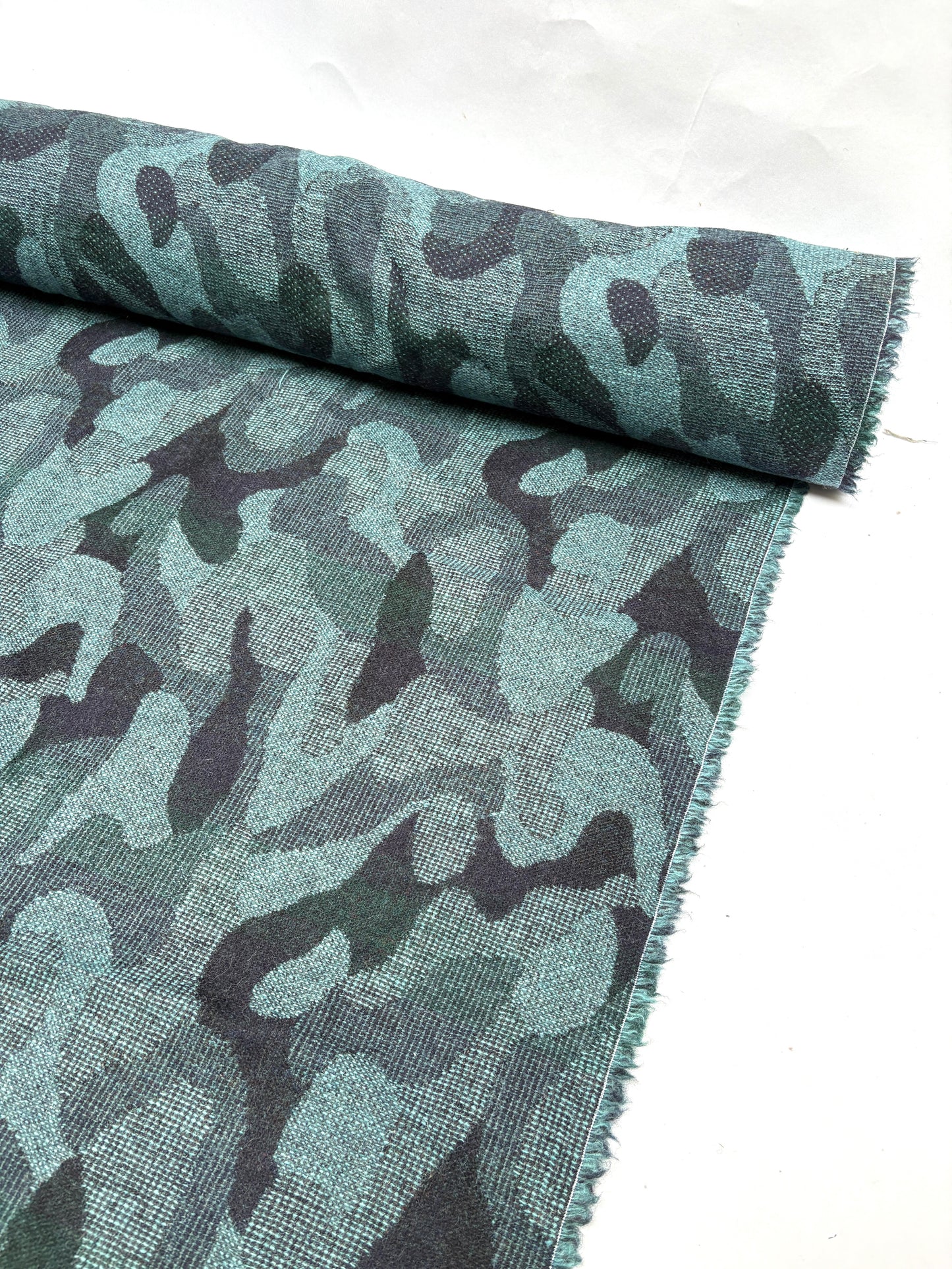 Close-up of a rolled camouflage-pattern jacquard-weave fabric in green and black with soft texture 