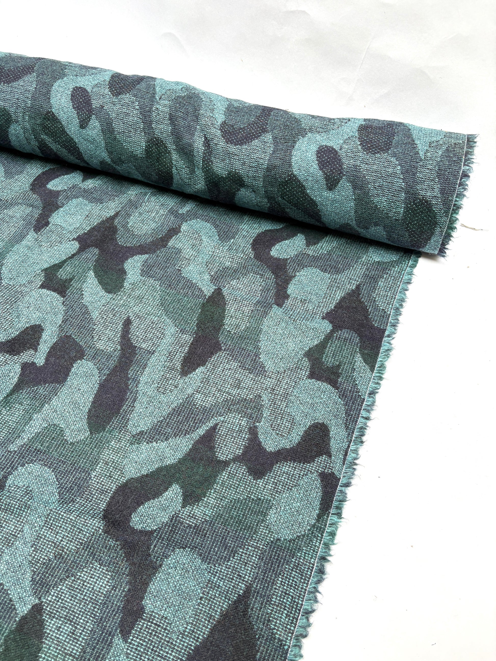 Close-up of a rolled camouflage-pattern jacquard-weave fabric in green and black with soft texture 