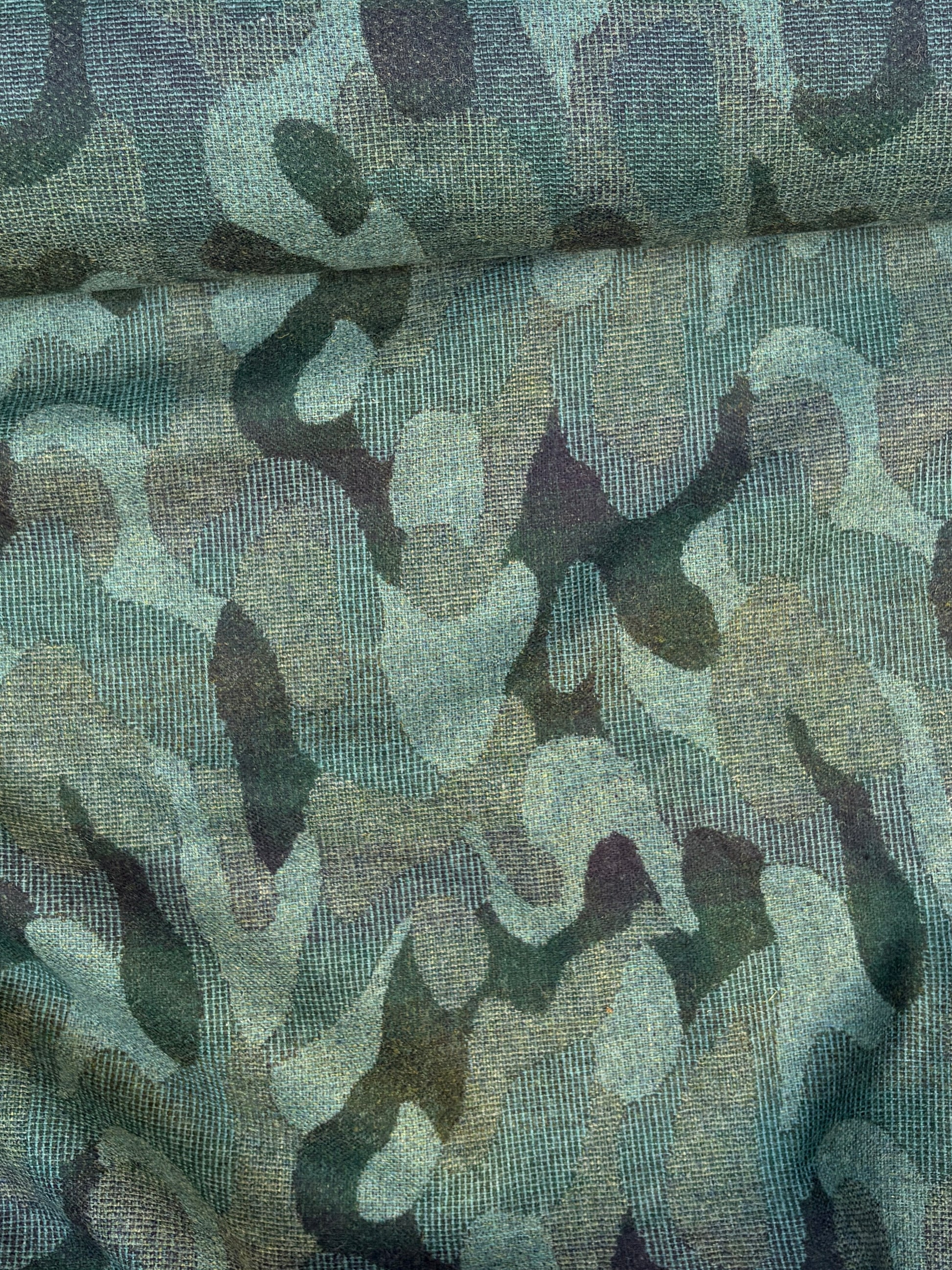 Close-up of a rolled camouflage-pattern jacquard-weave fabric in green and black with soft texture 