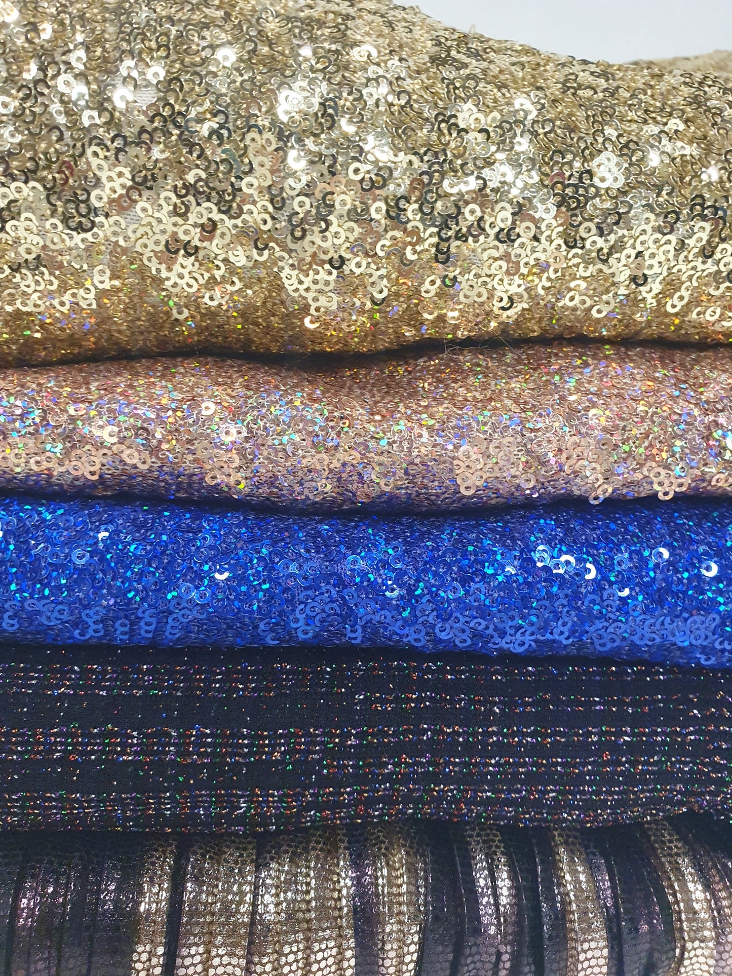 Close-up of a pile of folded glitter fabric with gold, pink, blue, and black