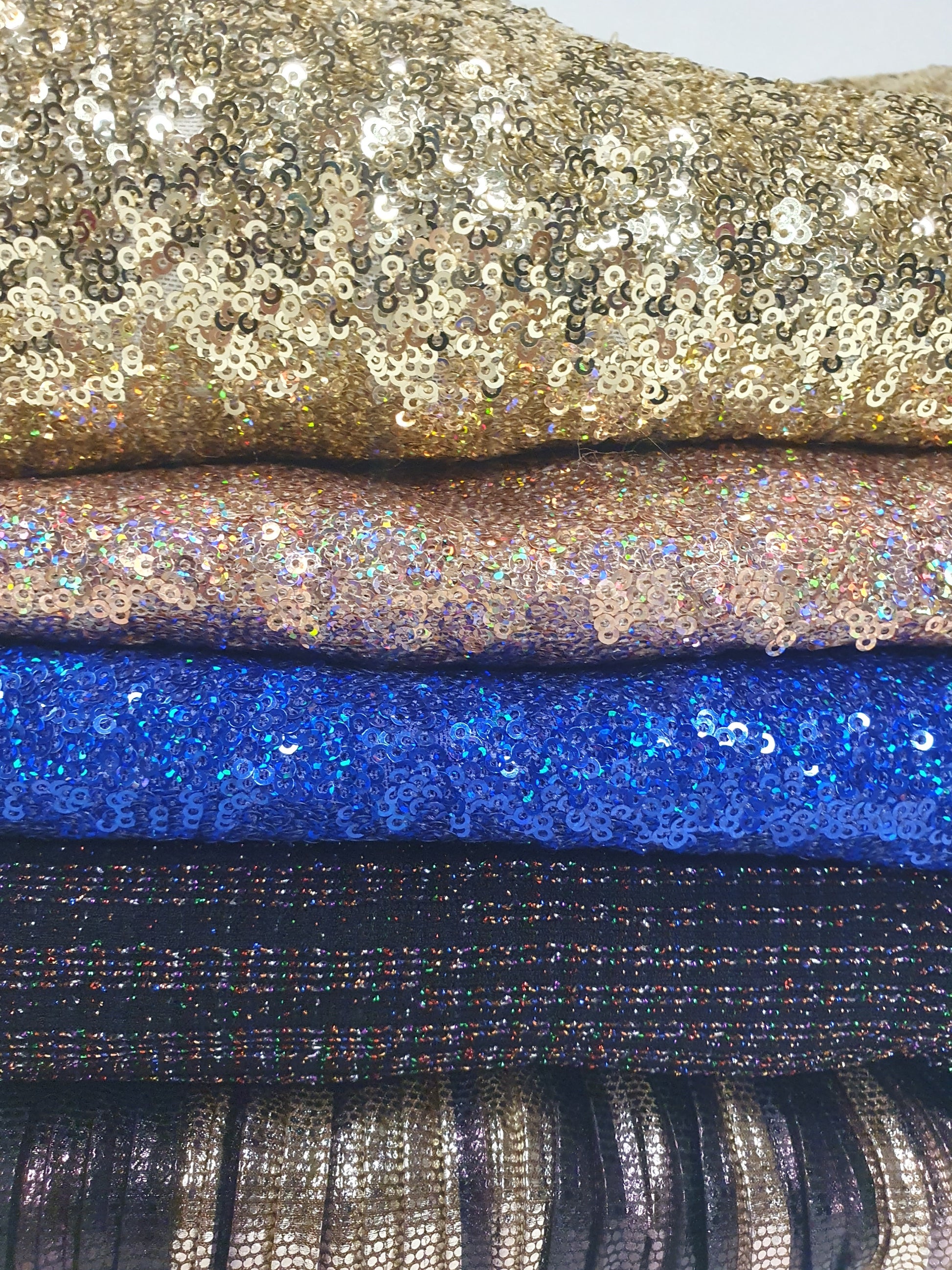 Close-up of a pile of folded glitter fabric with gold, pink, blue, and black