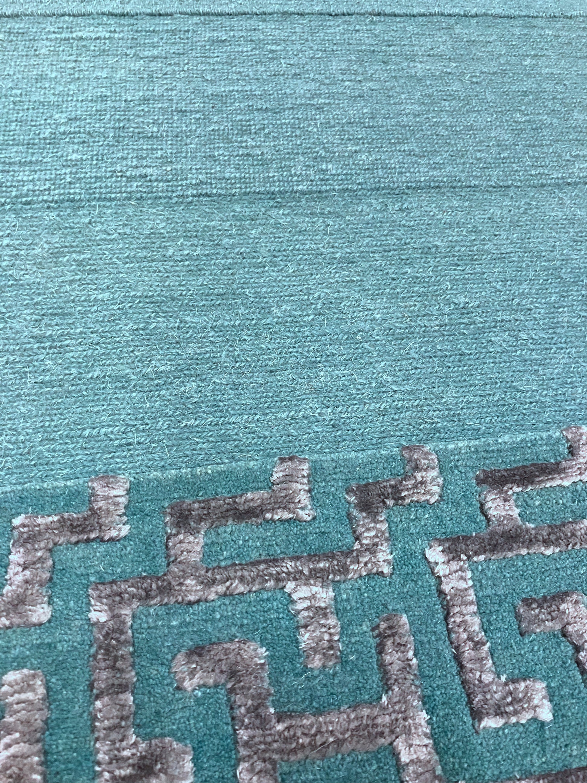 Close-up of hand knotted rug with green and silver geometric patterns 