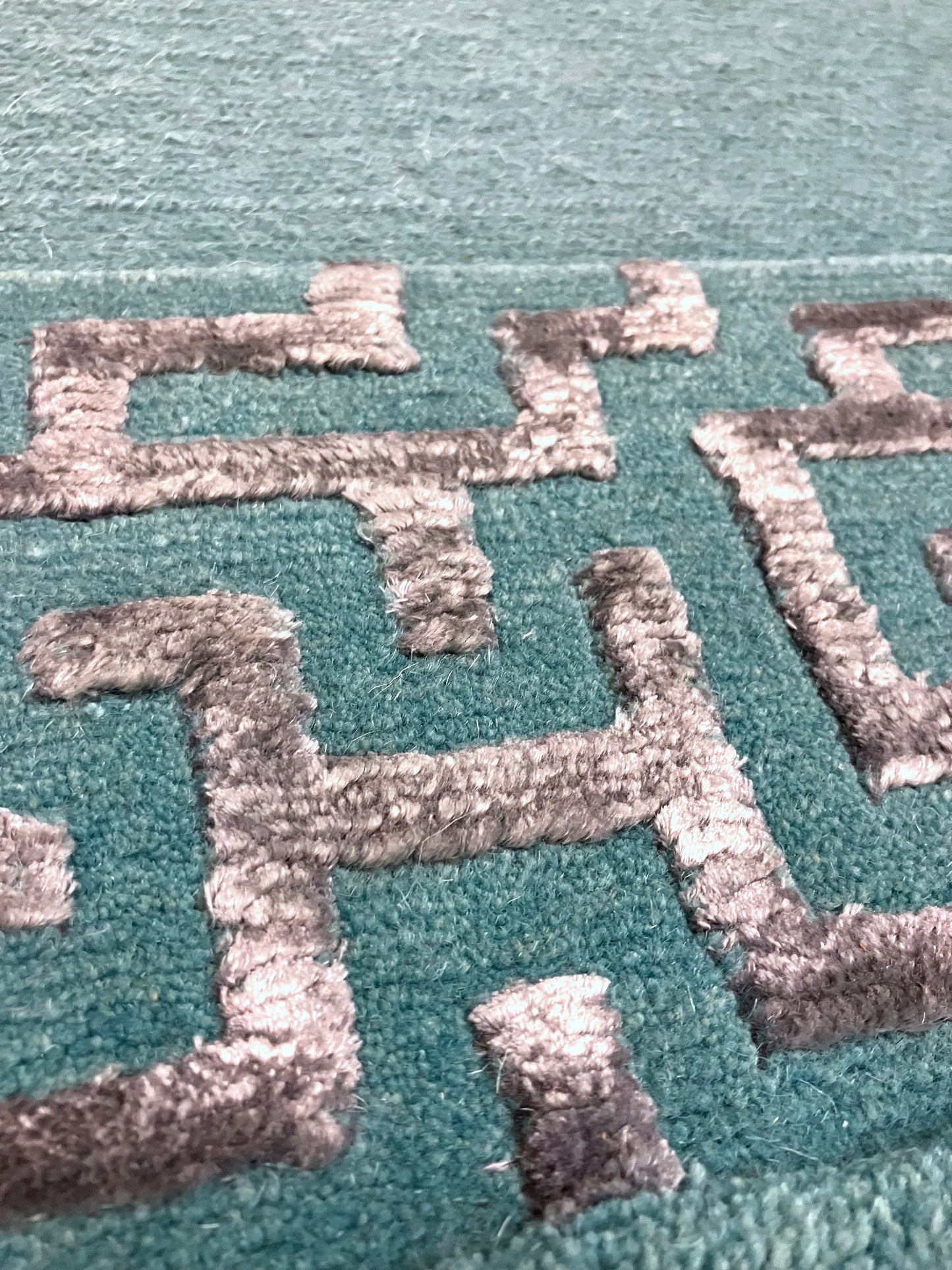 Close-up of hand knotted rug with green and silver geometric patterns 