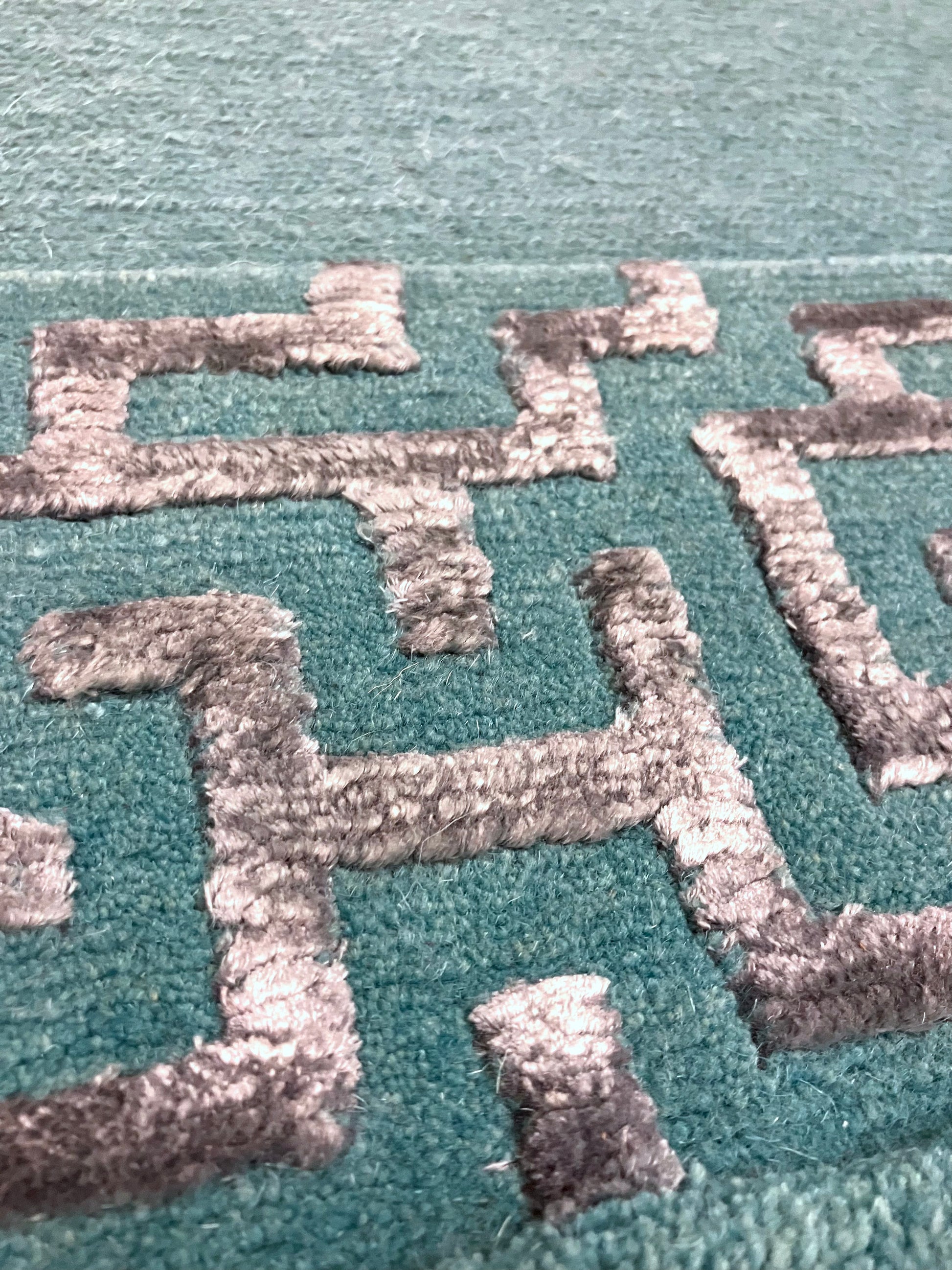 Close-up of hand knotted rug with green and silver geometric patterns 