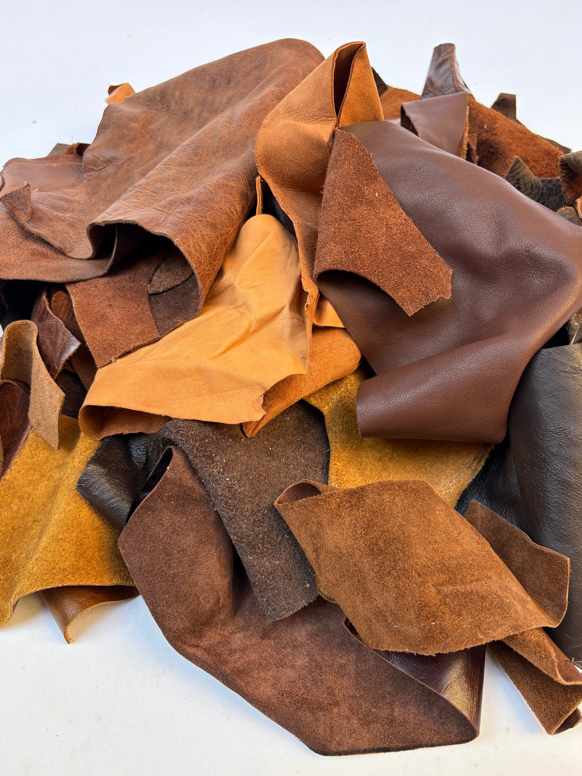 Close-up of a pile of various types of brown leather offcuts, soft texture visible