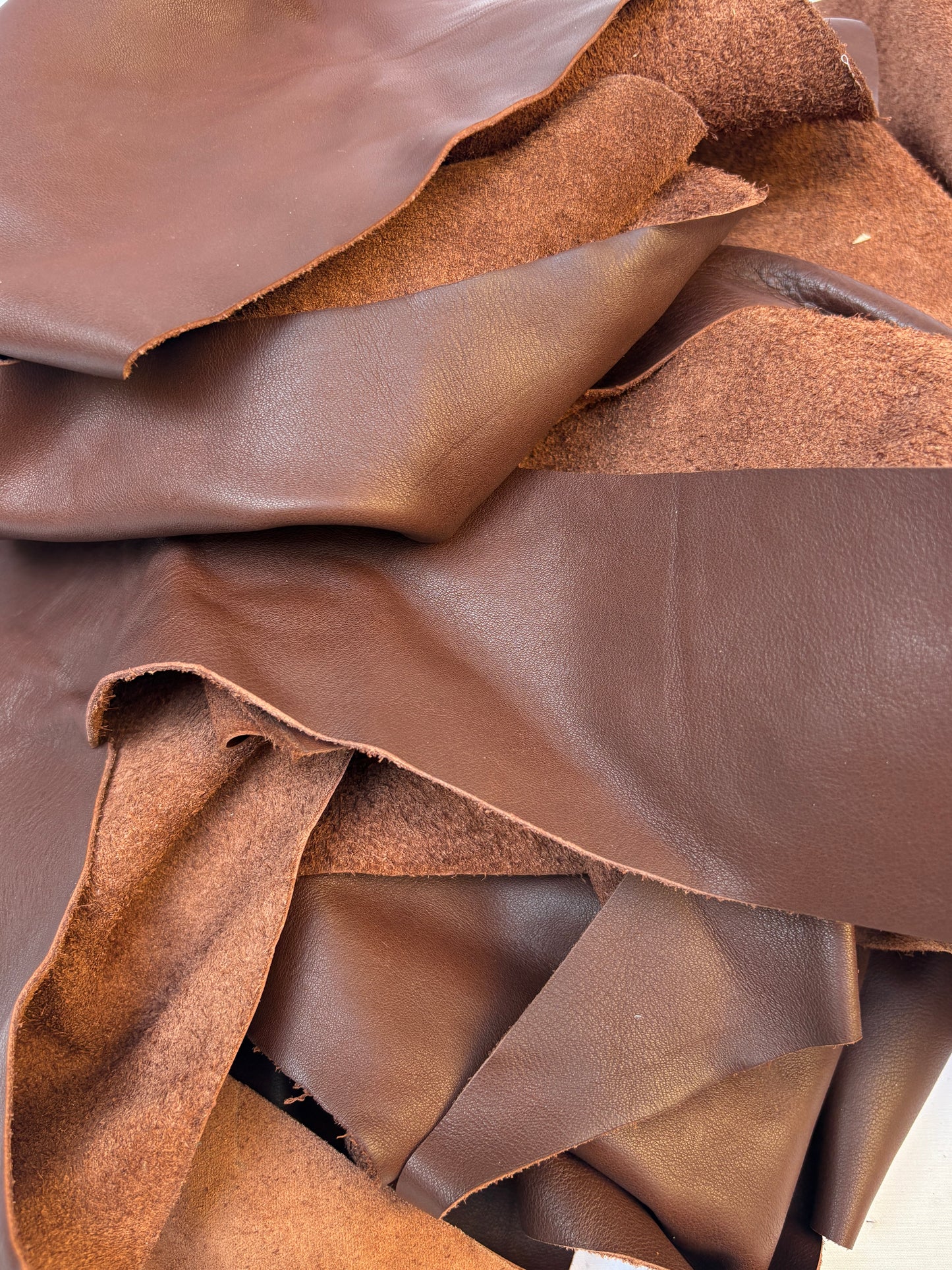 Close-up of a pile of light brown leather offcuts, shiny texture visible 