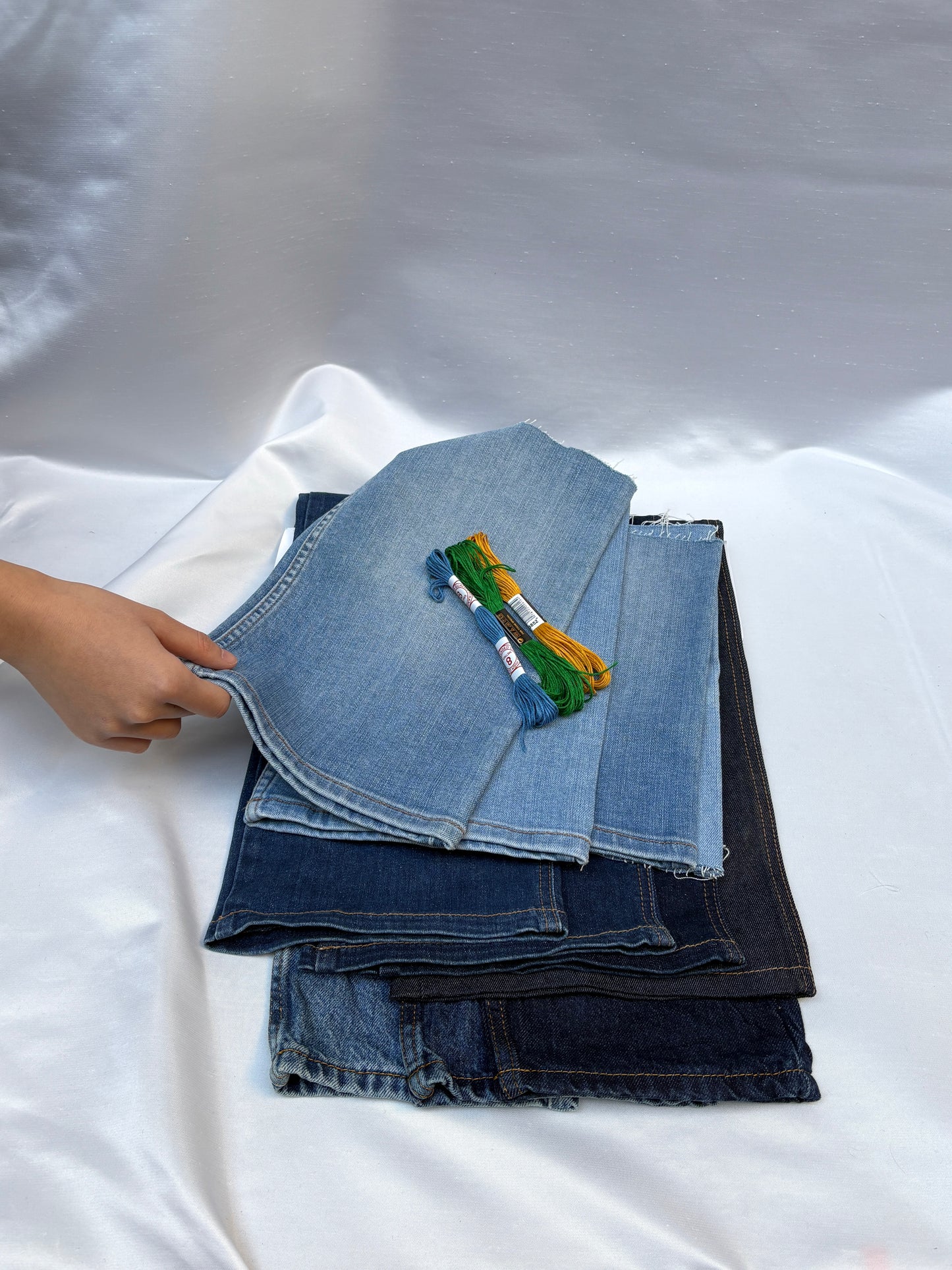 Stacked denim fabric pieces in mixed blue washes with embroidery threads.