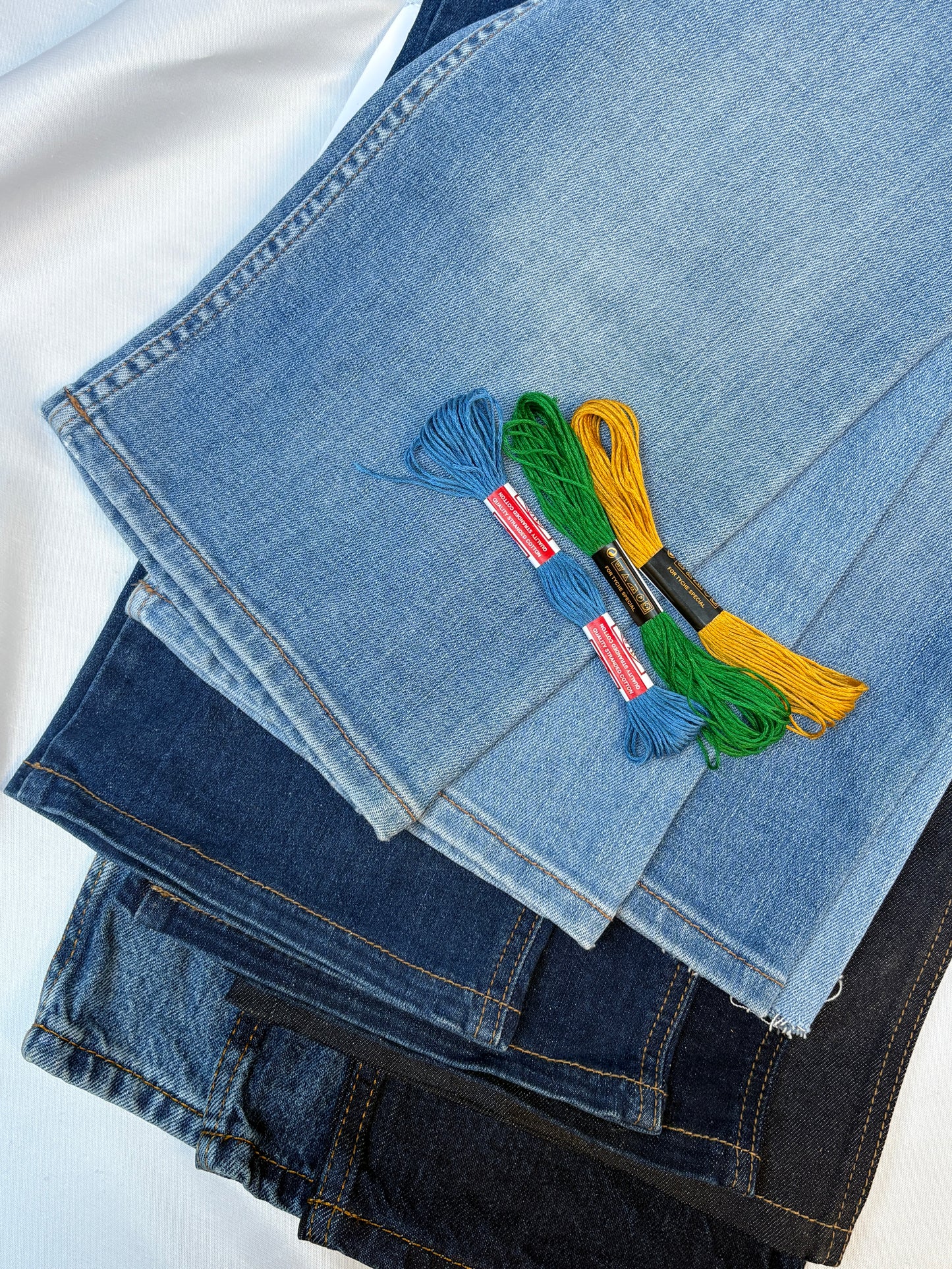 Layered denim fabric pieces with colourful embroidery threads in contrasting tones.
