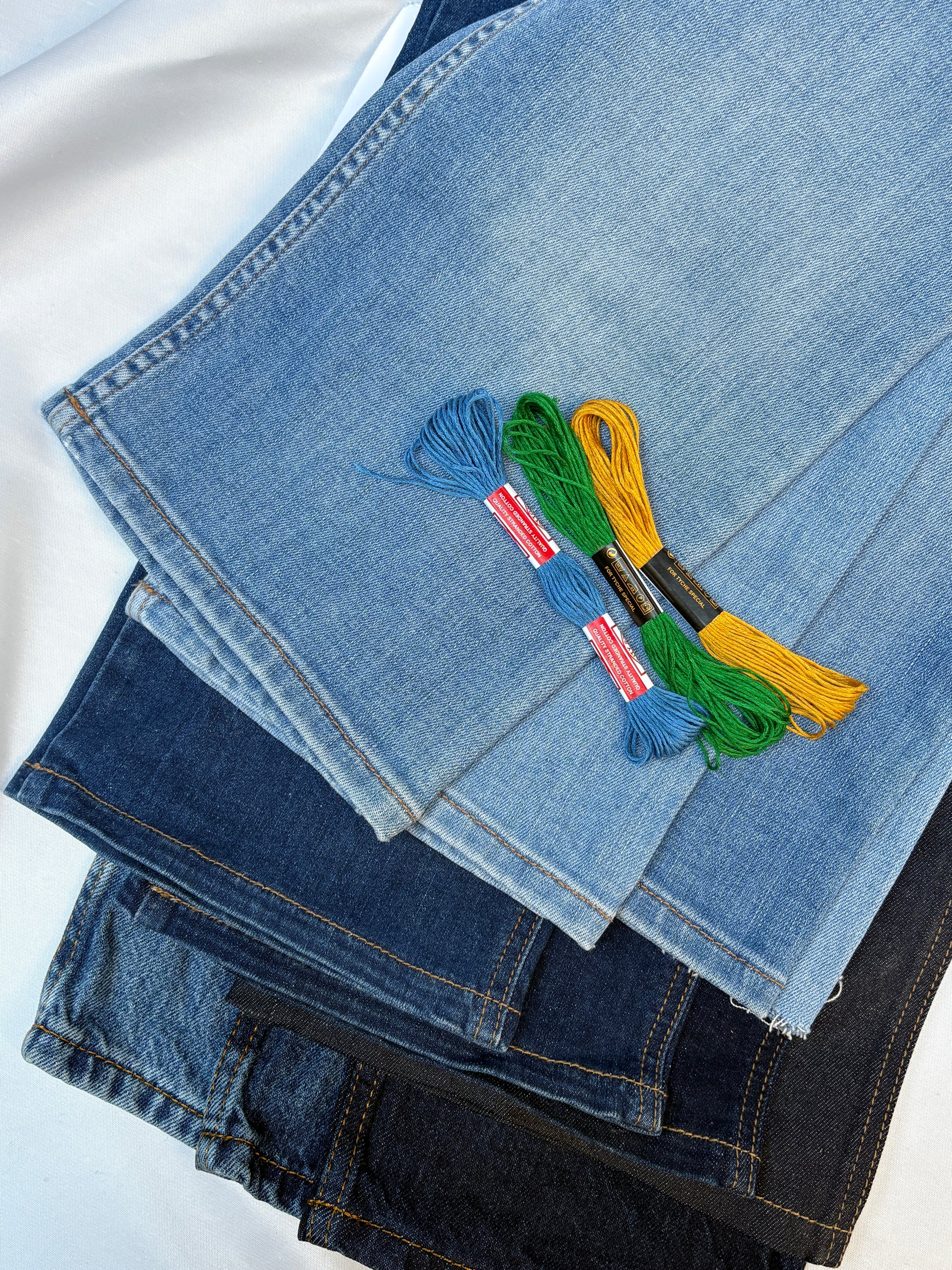 Layered denim fabric pieces with colourful embroidery threads in contrasting tones.