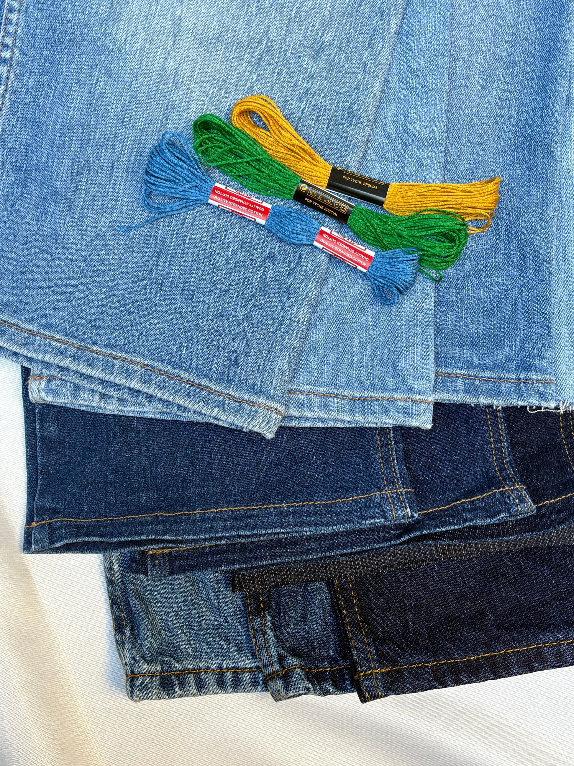 Stacked denim pieces in mixed blue washes with colourful embroidery threads.