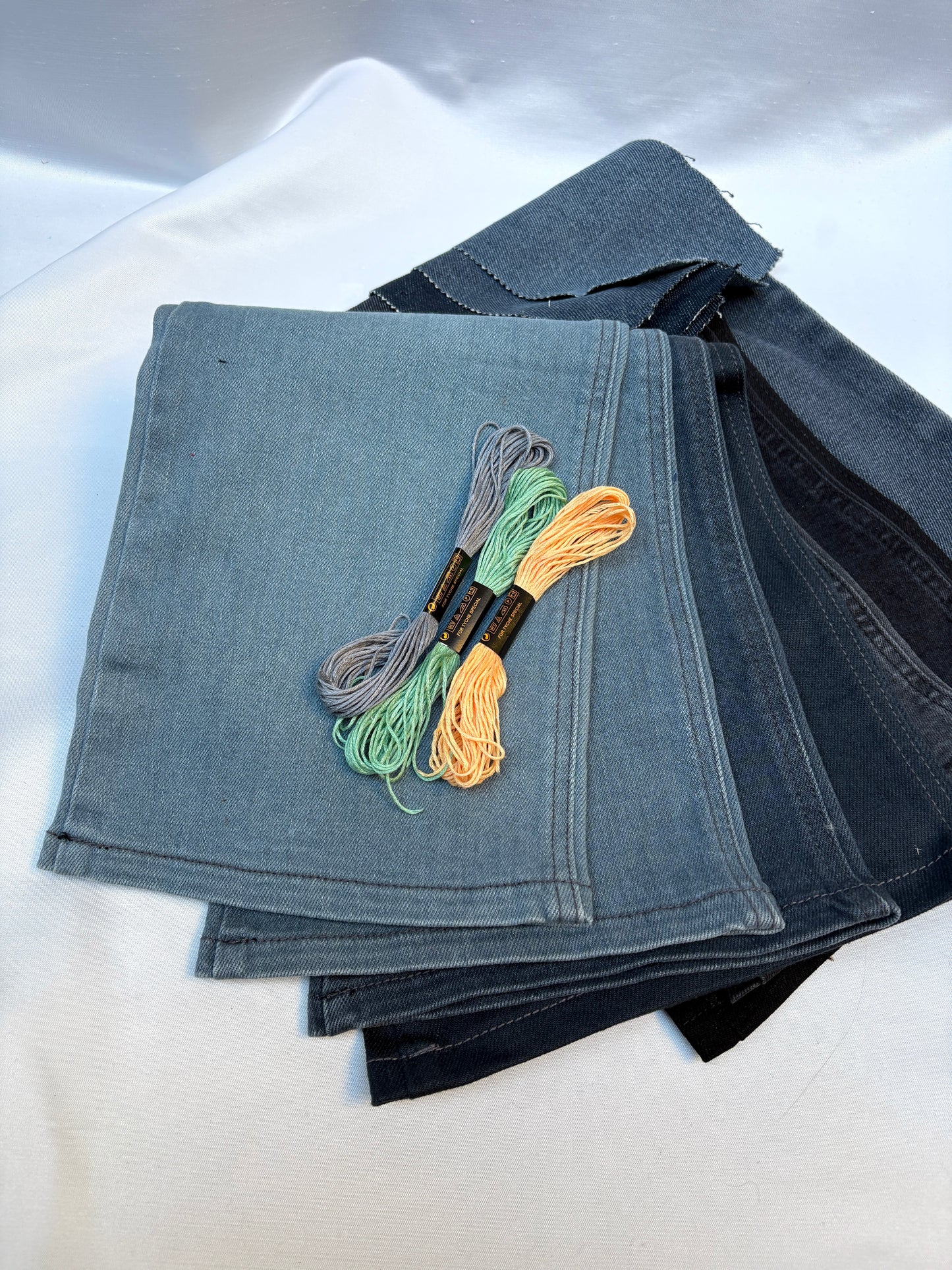 Stacked denim fabric pieces in mixed washes with colourful embroidery threads.