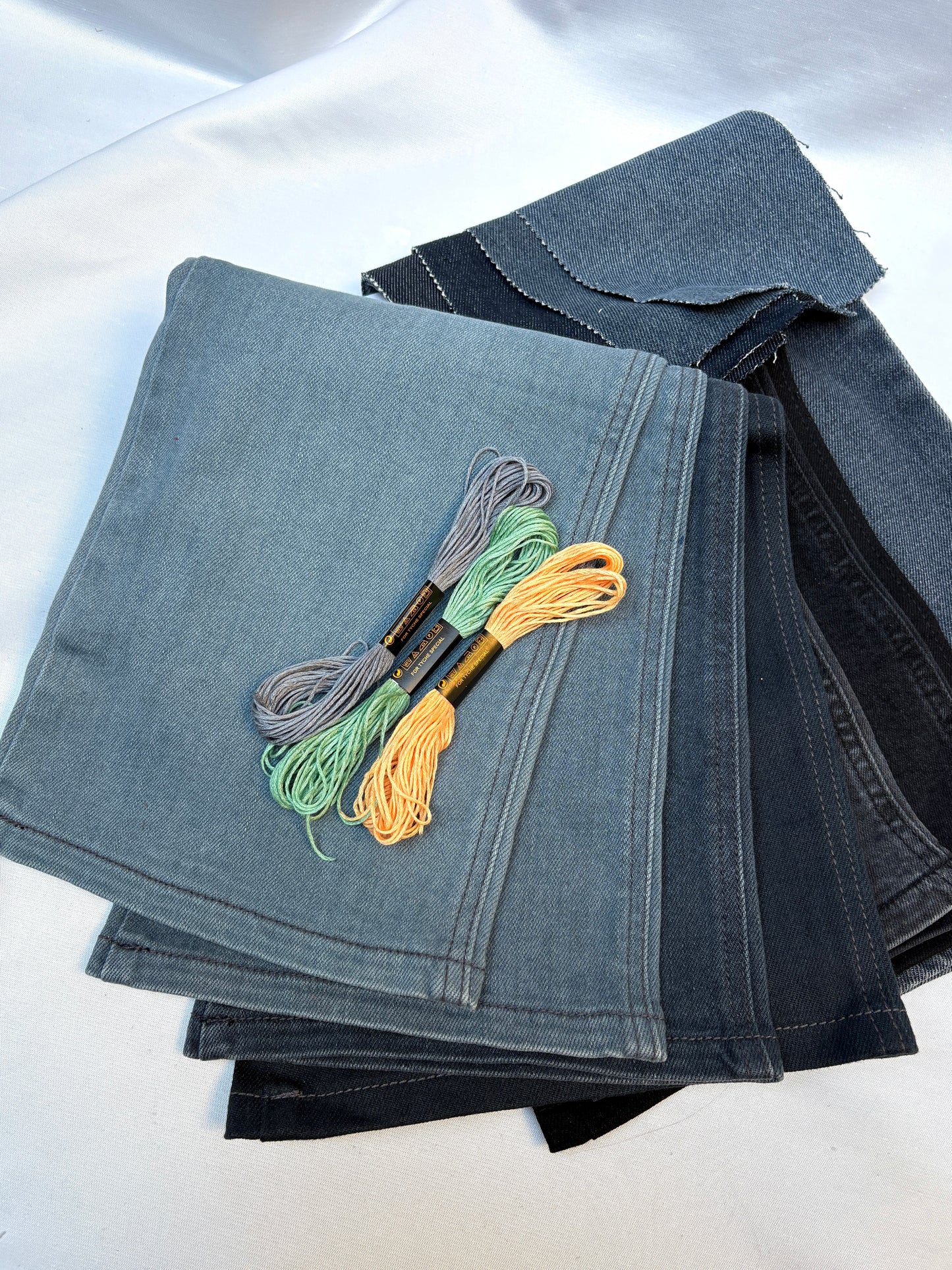 Layered denim fabric pieces with embroidery threads in soft contrasting colours.