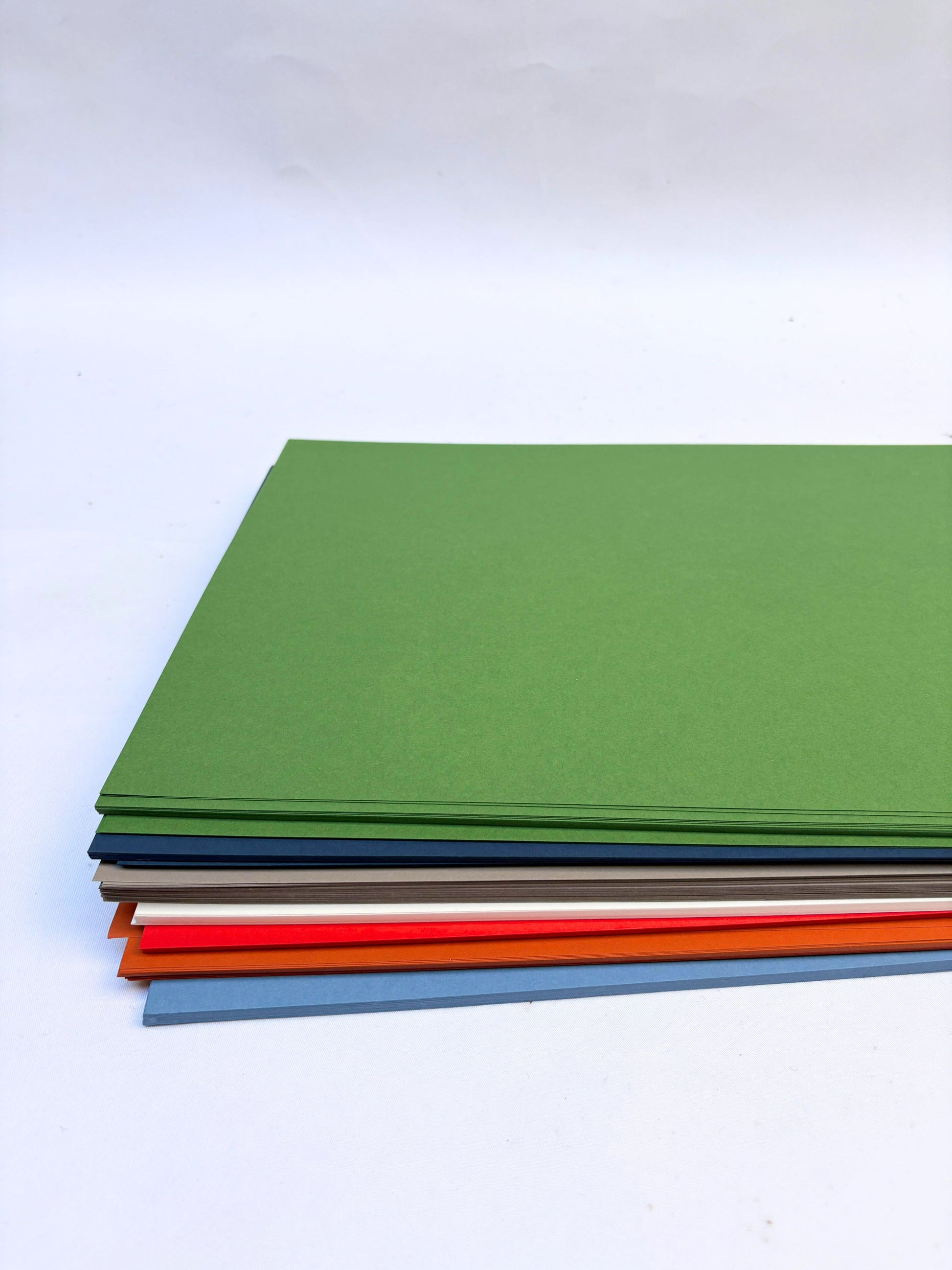 Stack of coloured papers, green, dark blue, grey, white, red, orange, and blue