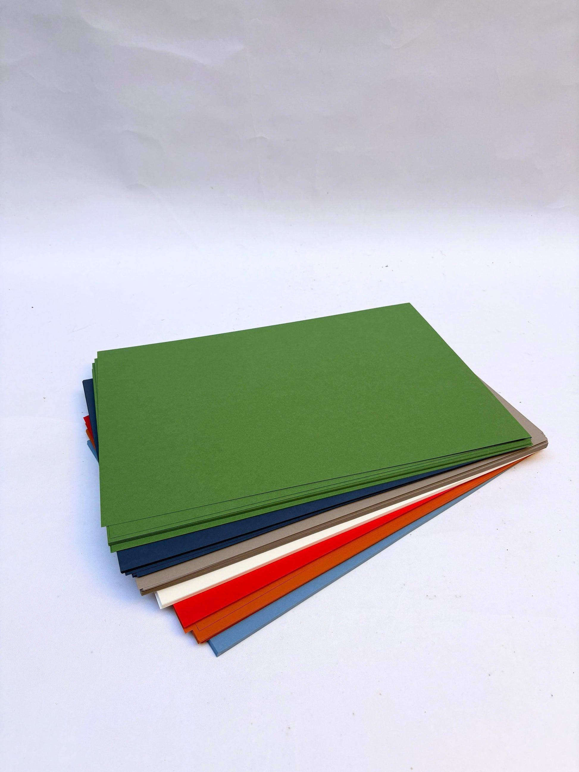 Stack of coloured papers, green, dark blue, grey, white, red, orange, and blue