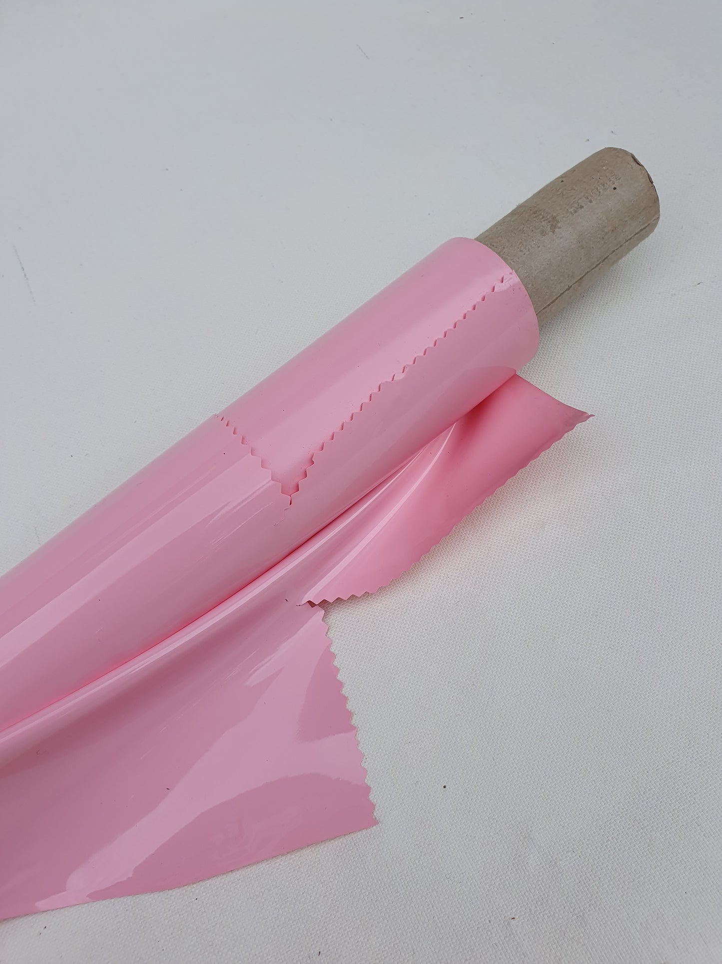 Close-up of a pink rolled-up shiny plastic film with partially cut edge 