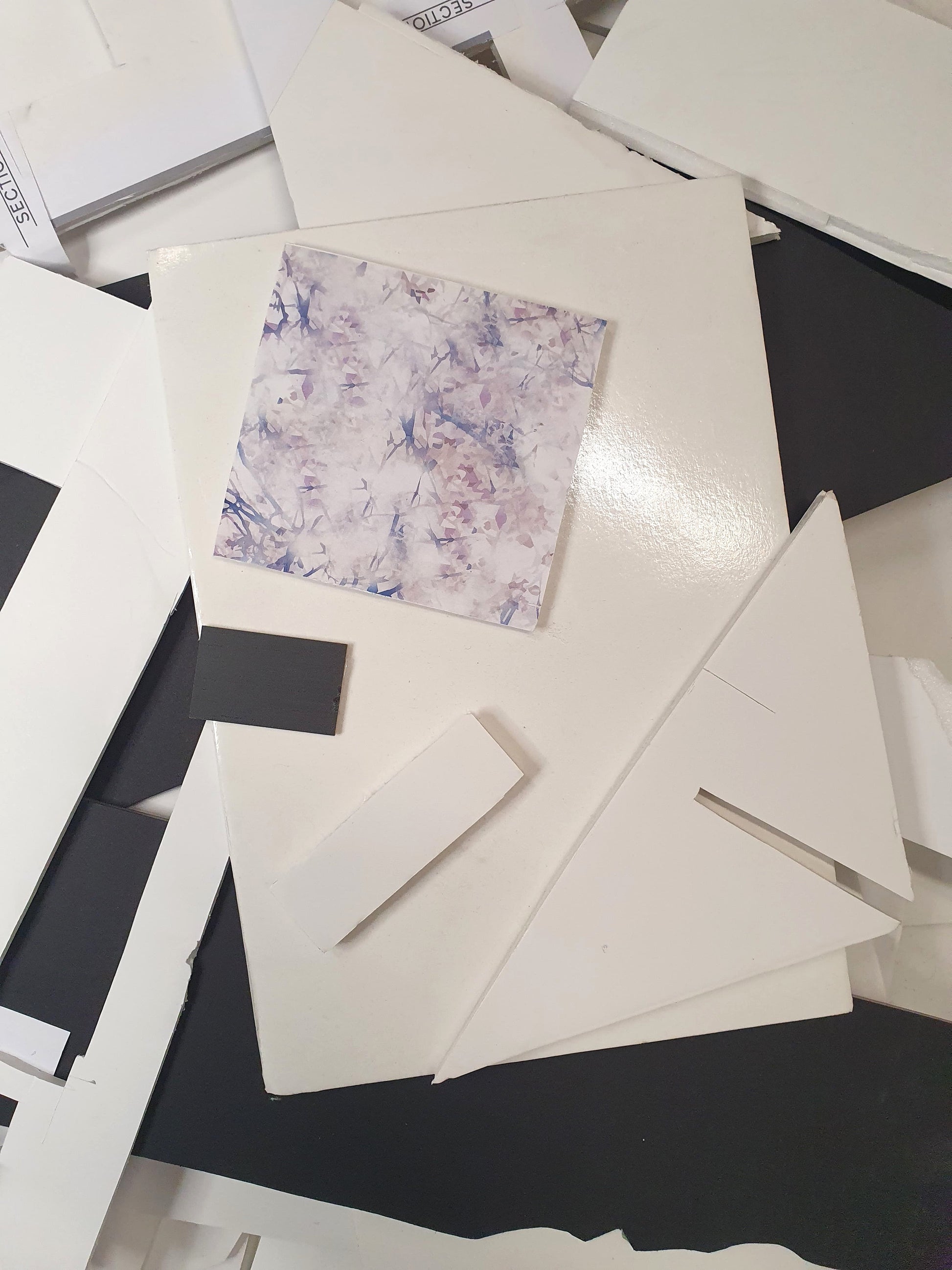 A patterned square plastic foam board on top of a collection of black and white foam board offcuts of various sizes