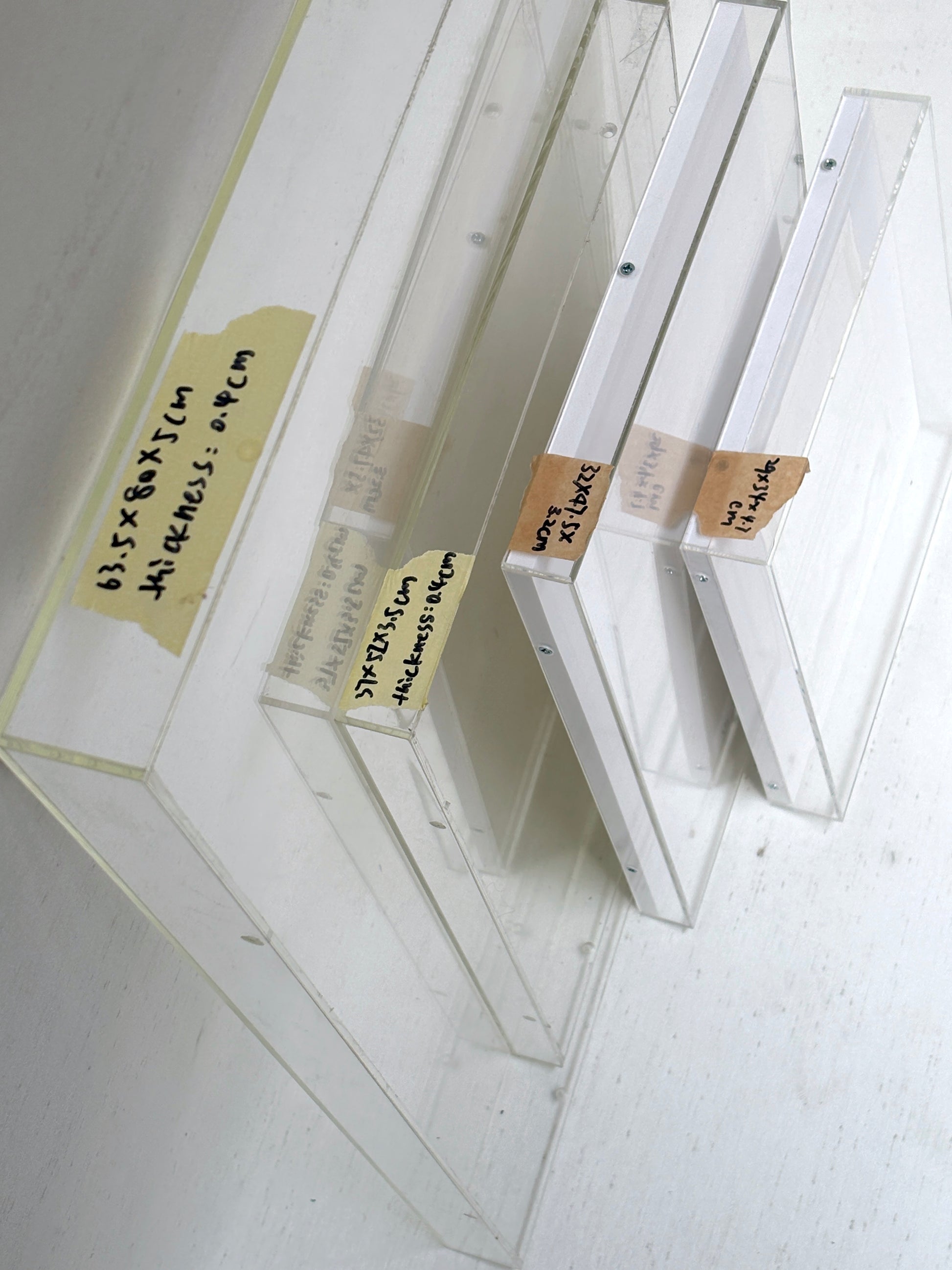 A collection of 4 varying sizes of the clear rectangular perspex frames with a tape stating each size