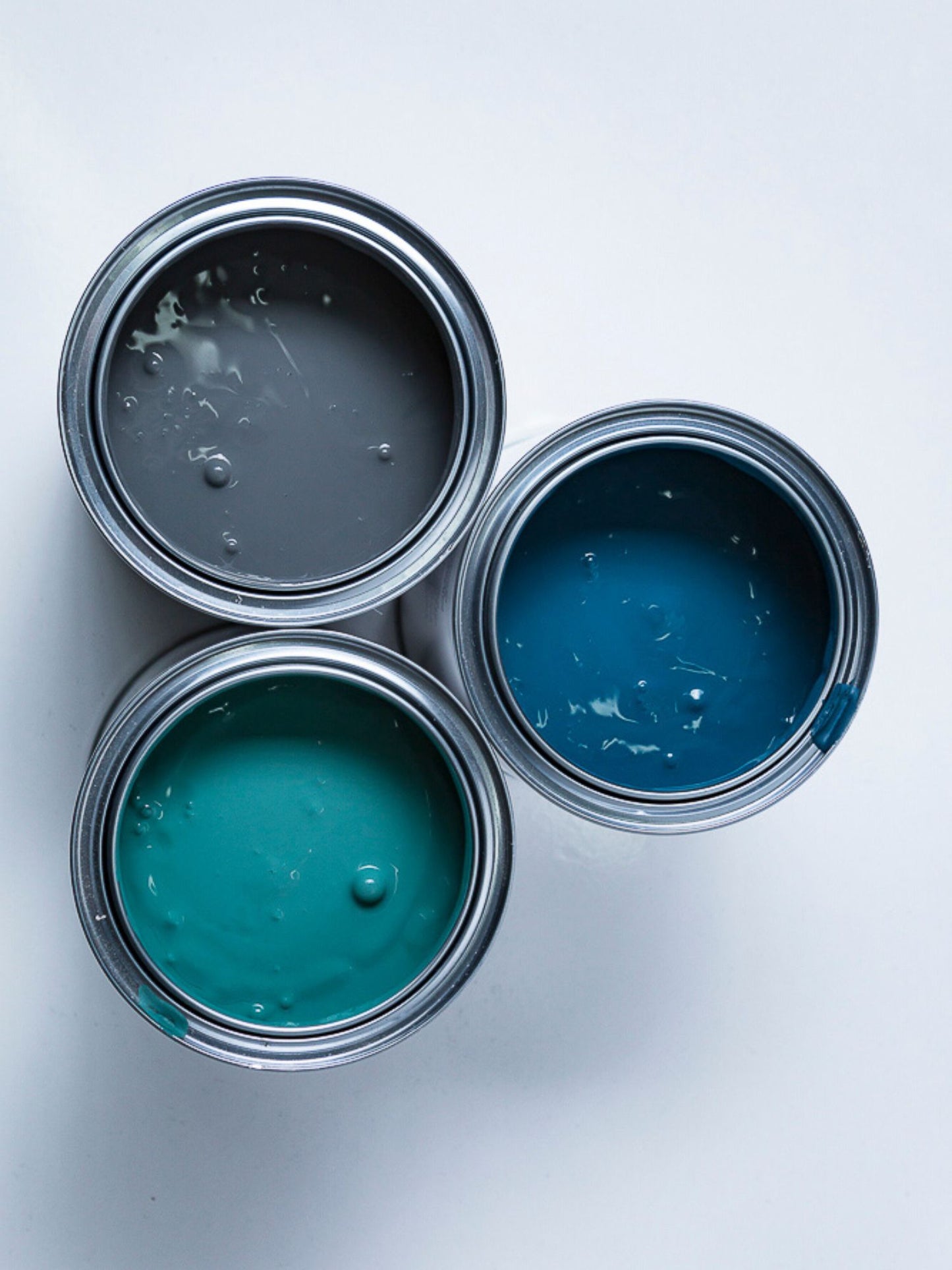 Three open paint cans with different blue shades of chalky acrylic paint.