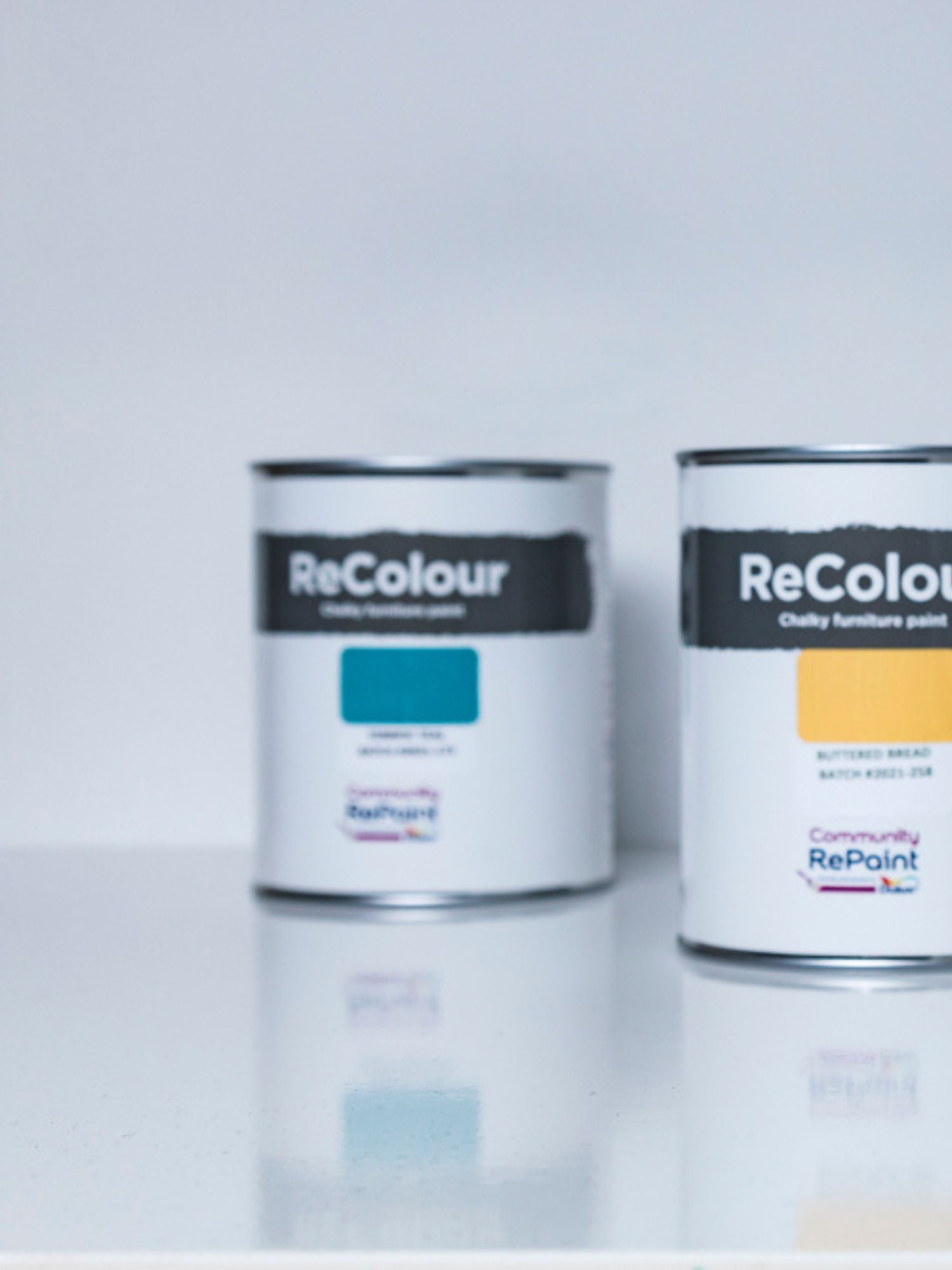 Two cans of ReColour acrylic chalky furniture paint, one blue and one yellow paint.