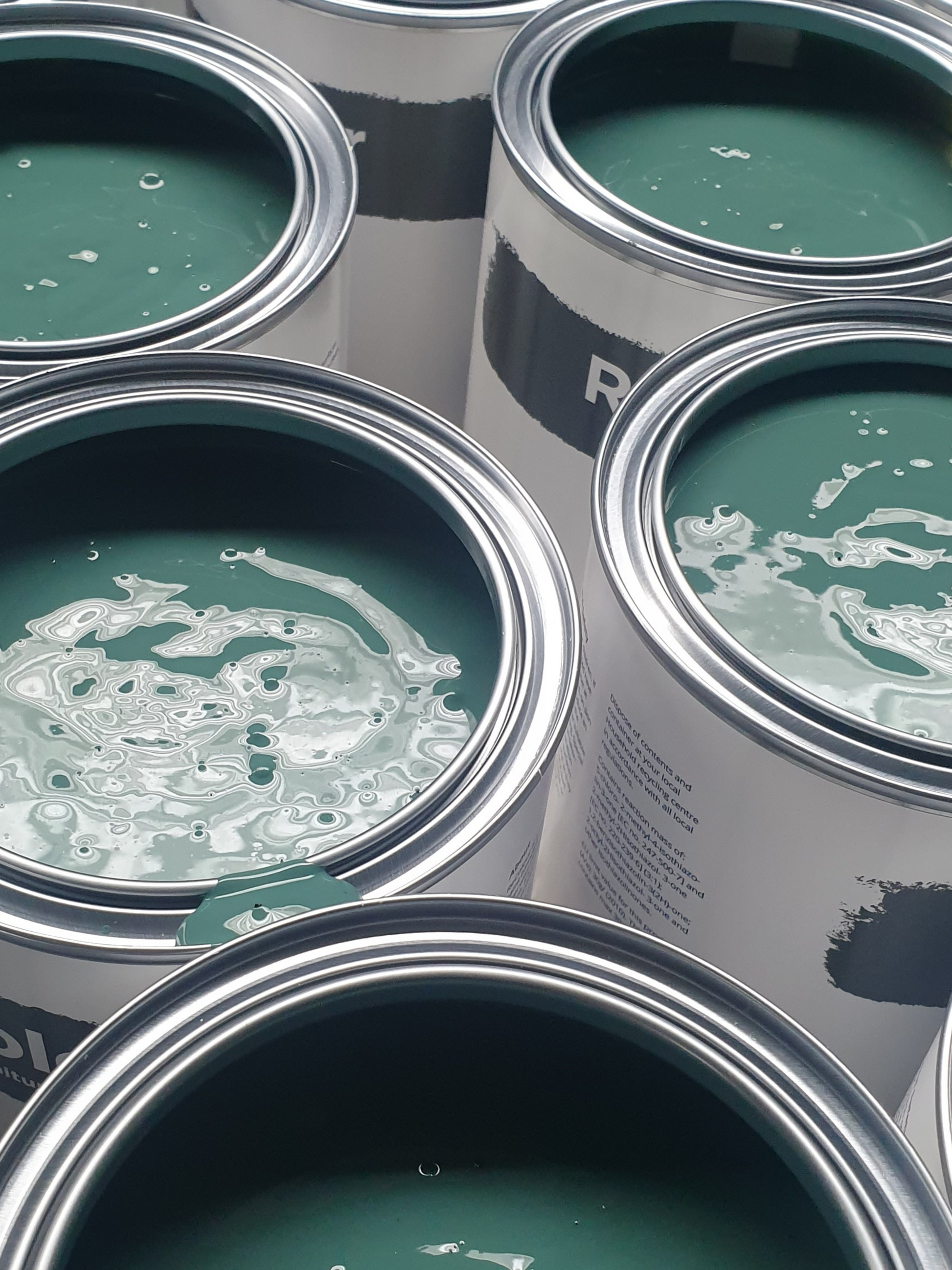 Close-up of multiple open cans of dark green paint.