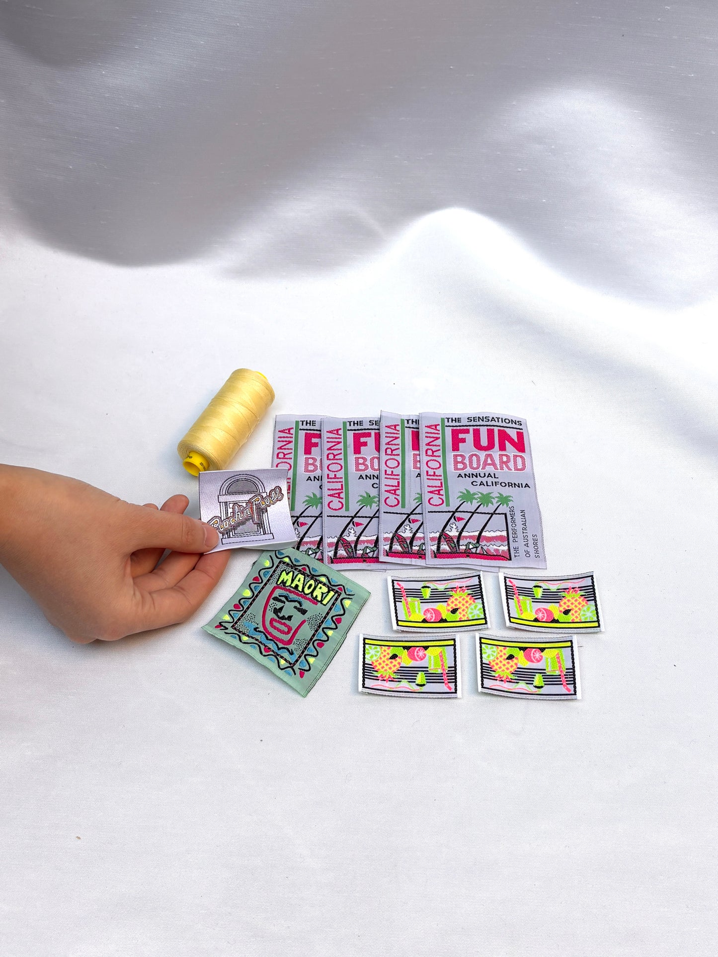 Hand holding woven labels and badges beside a yellow thread spool.