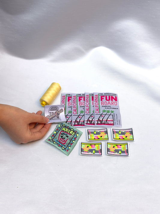 Hand holding woven labels and badges beside a yellow thread spool.