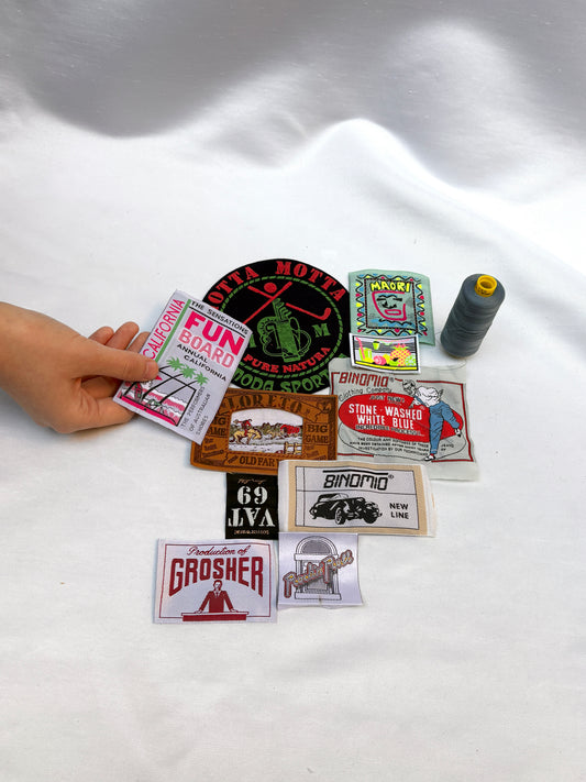 Assorted woven badges and labels displayed with a hand and thread spool.