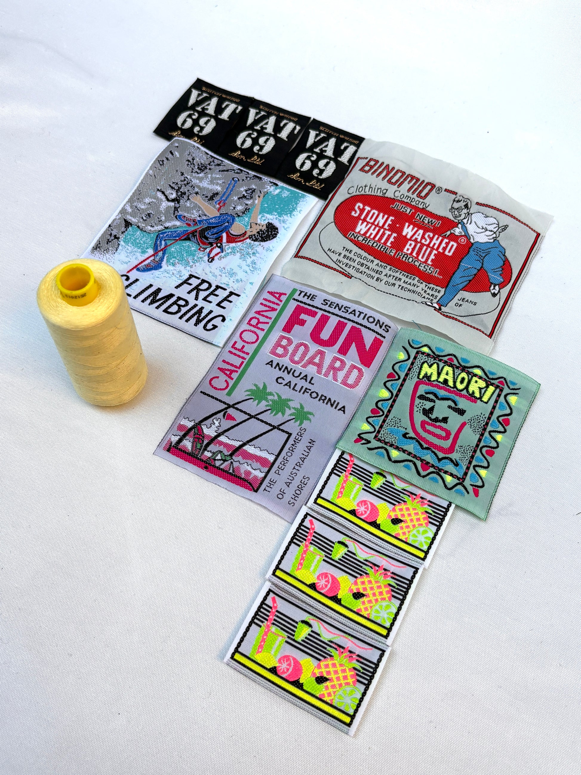 A selection of vintage-style product labels with a yellow thread spool on white fabric.