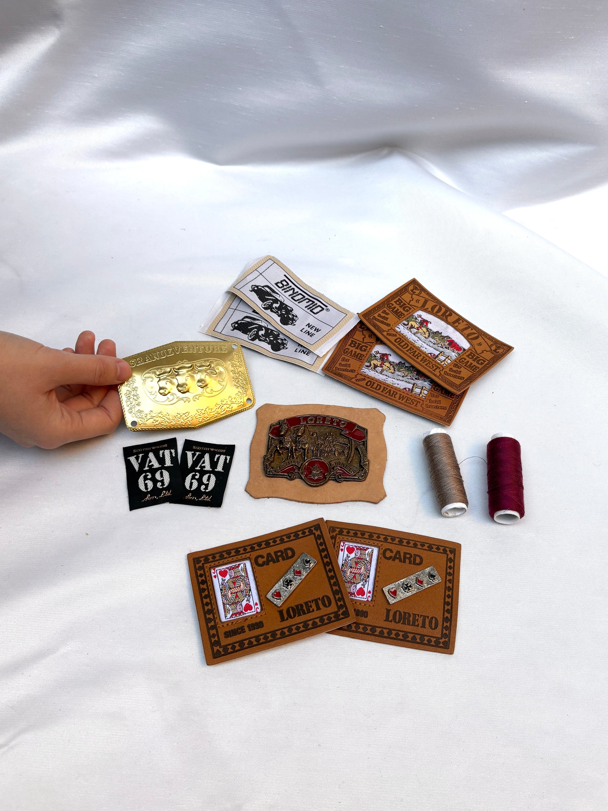 Vintage-style woven labels and badges arranged with thread spools on white fabric.
