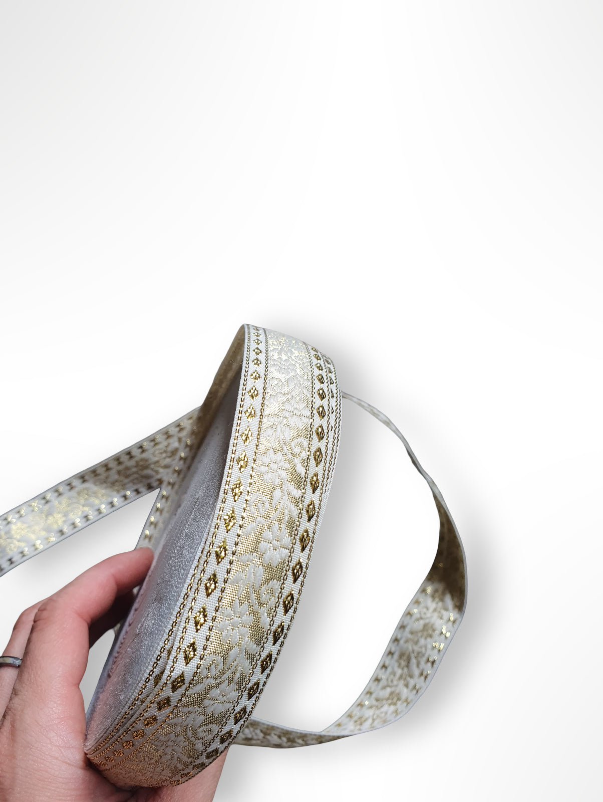 Hand holding a roll of floral embroidered ribbon with gold and white colours