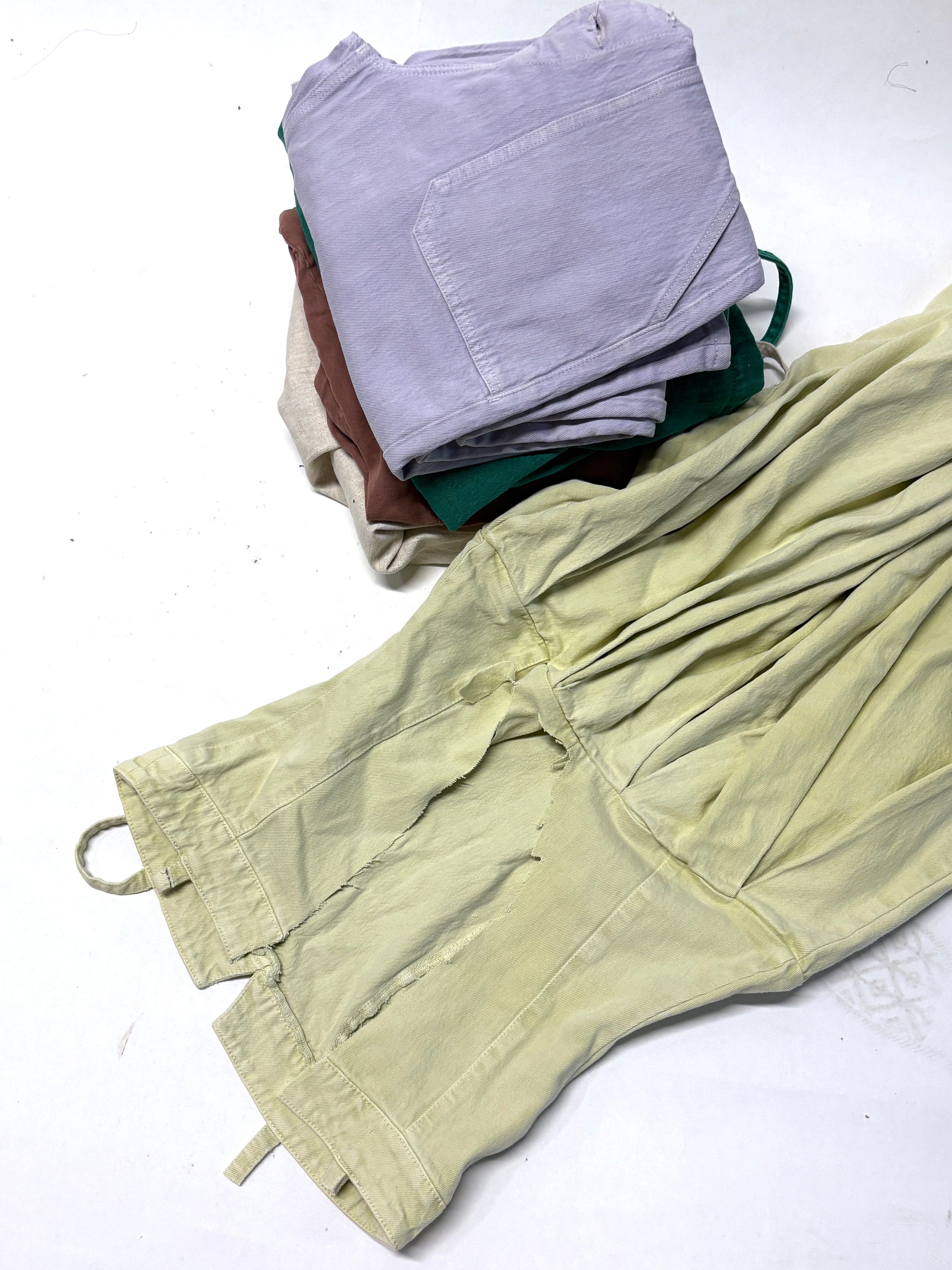 A yellow ripped denim garment and a stack of folded ripped denim garments 