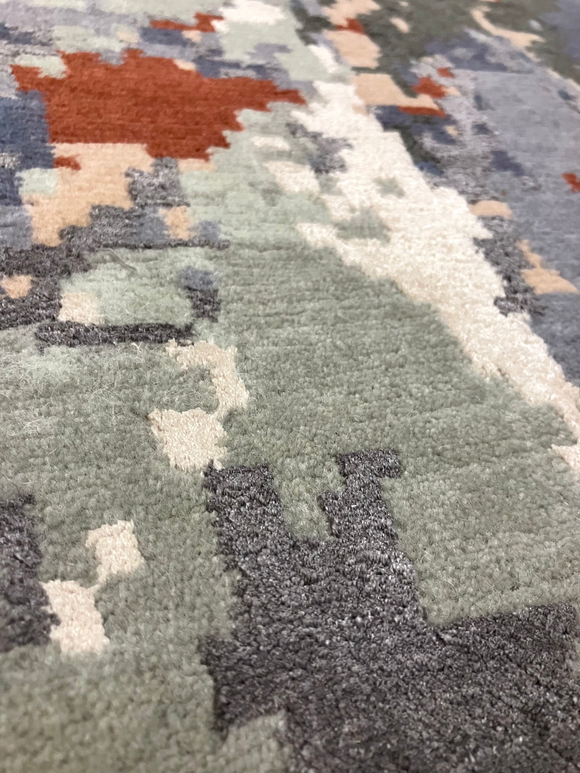 Close-up of a hand knotted Cascade rug with a geometric pattern in shades of blue, gray, and red, with visible textures