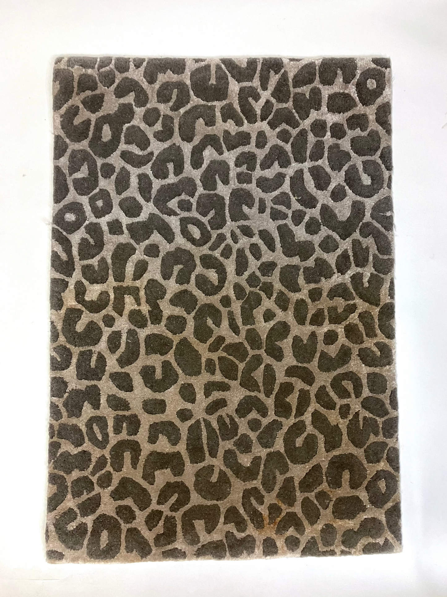 A rectangular, hand knotted wool rug with a leopard animal print pattern in shades of brown and beige.