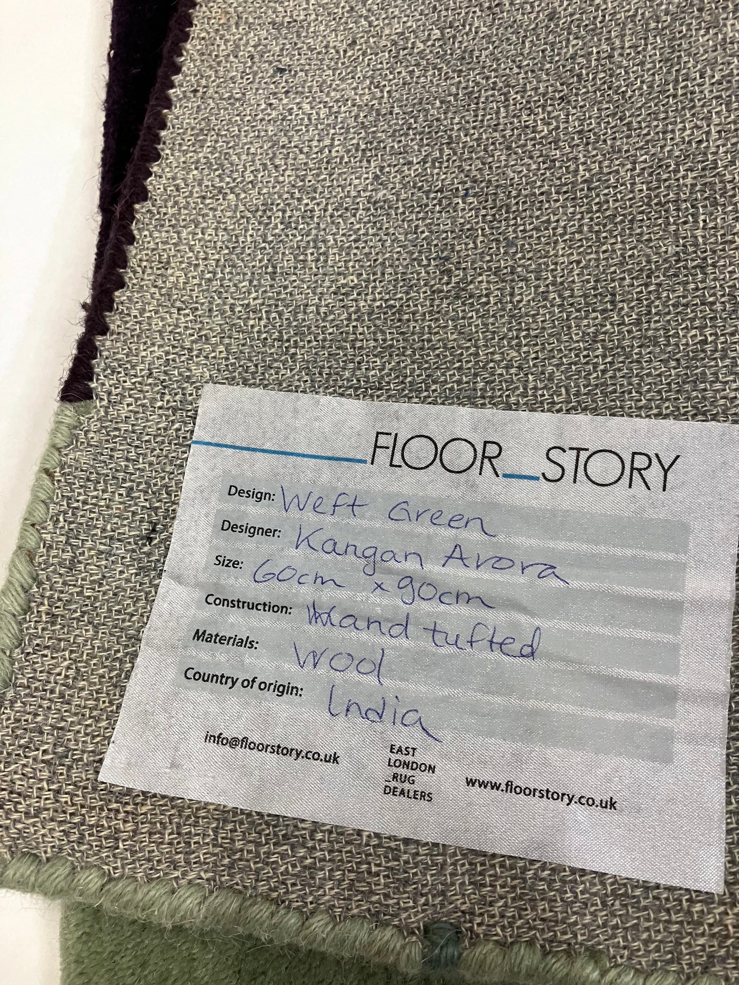Close-up of the back of a hand tufted wool rug with visible texture, with a sticker that contains the content of the rug
