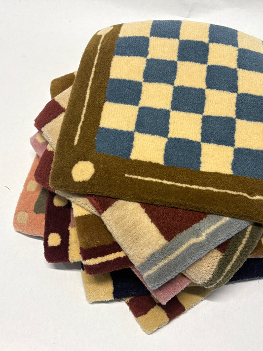Stack of different colours of square/jack patterned rug samples on a white background