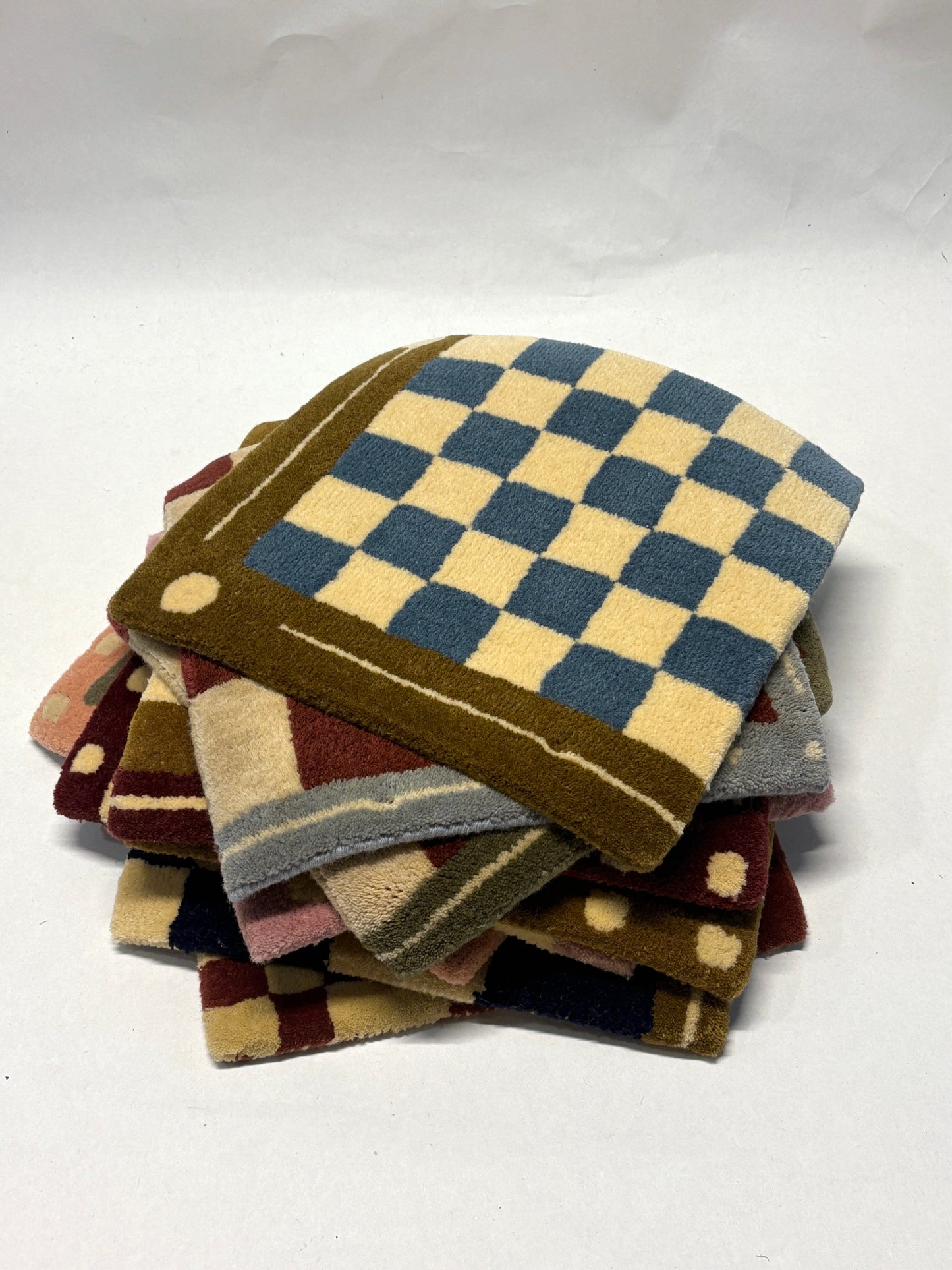 Stack of different colours of square/jack patterned rug samples.