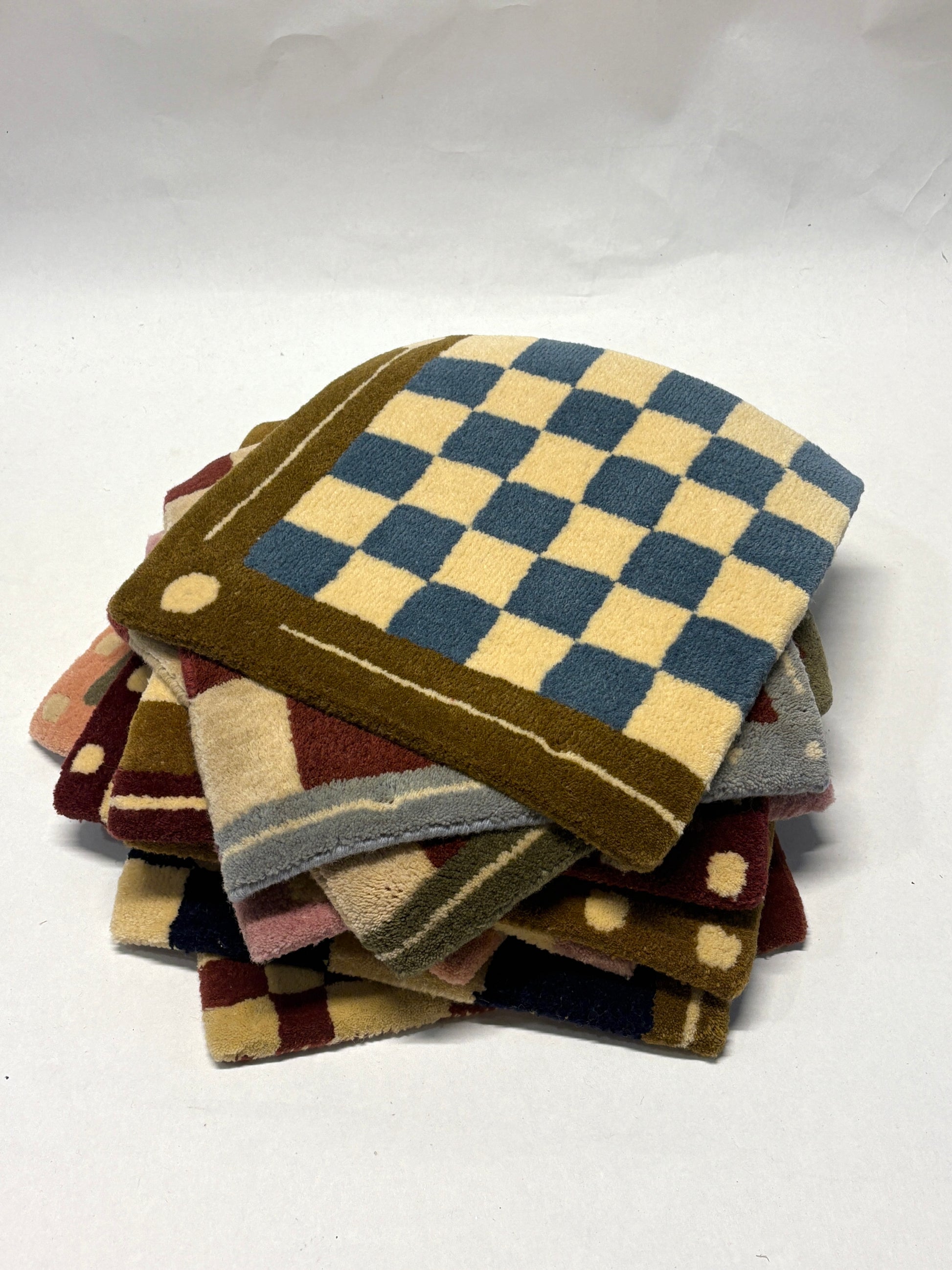 Stack of different colours of square/jack patterned rug samples.