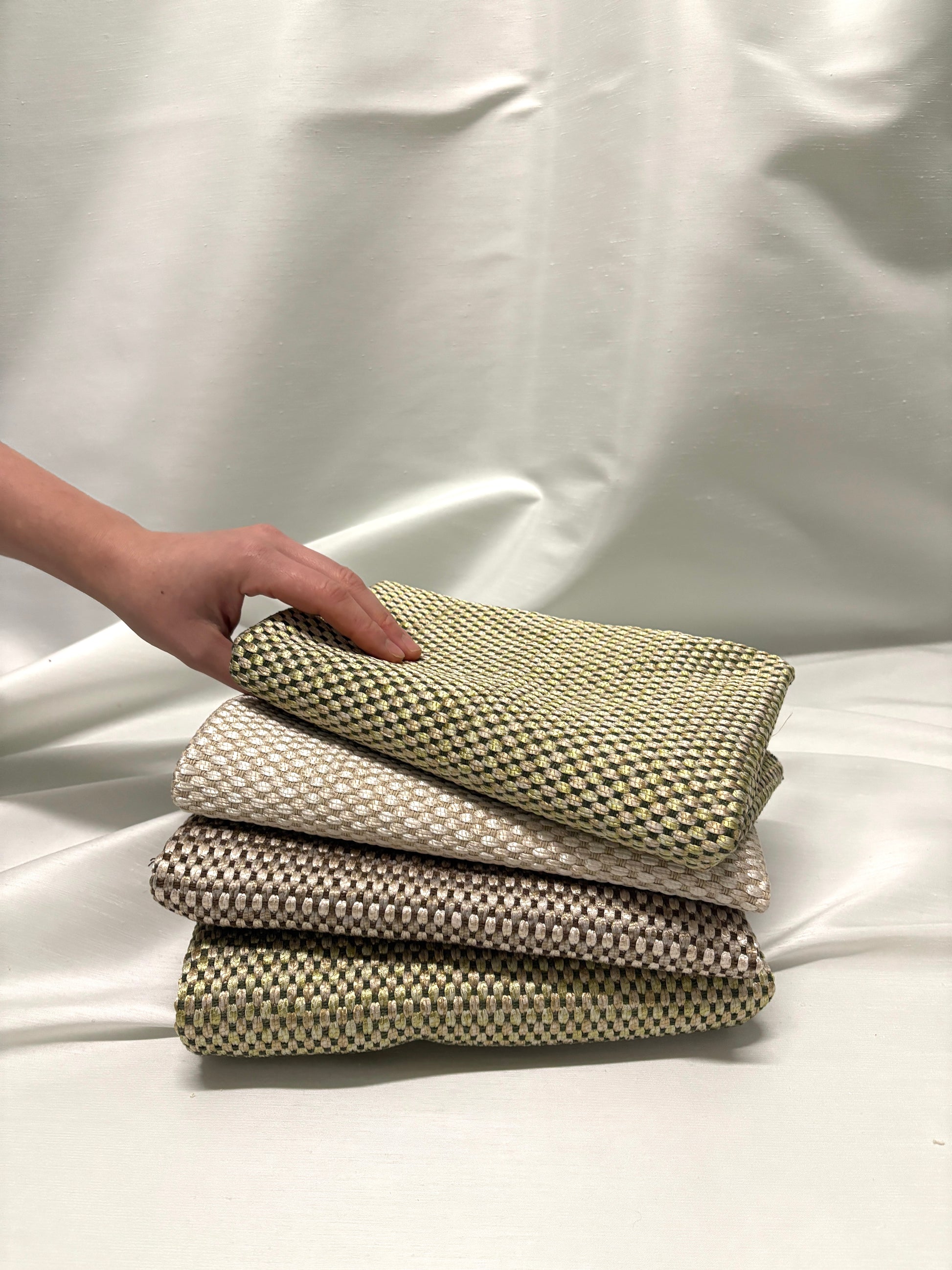 Hand holding stacked woven fabric swatches in soft neutral tones.