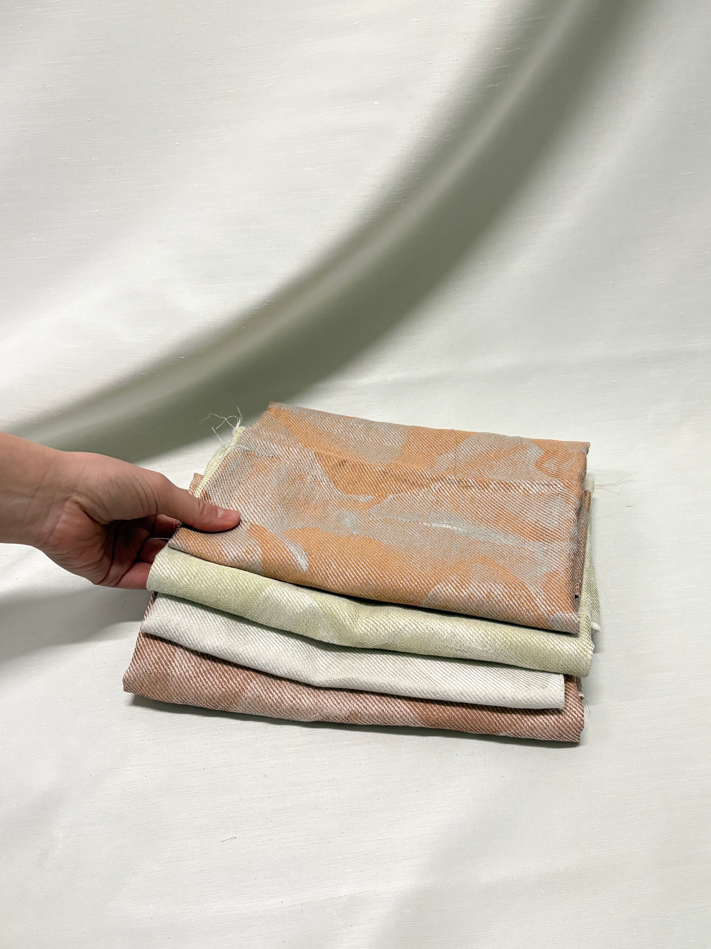 Hand holding stacked neutral fabric swatches in soft beige and cream tones.