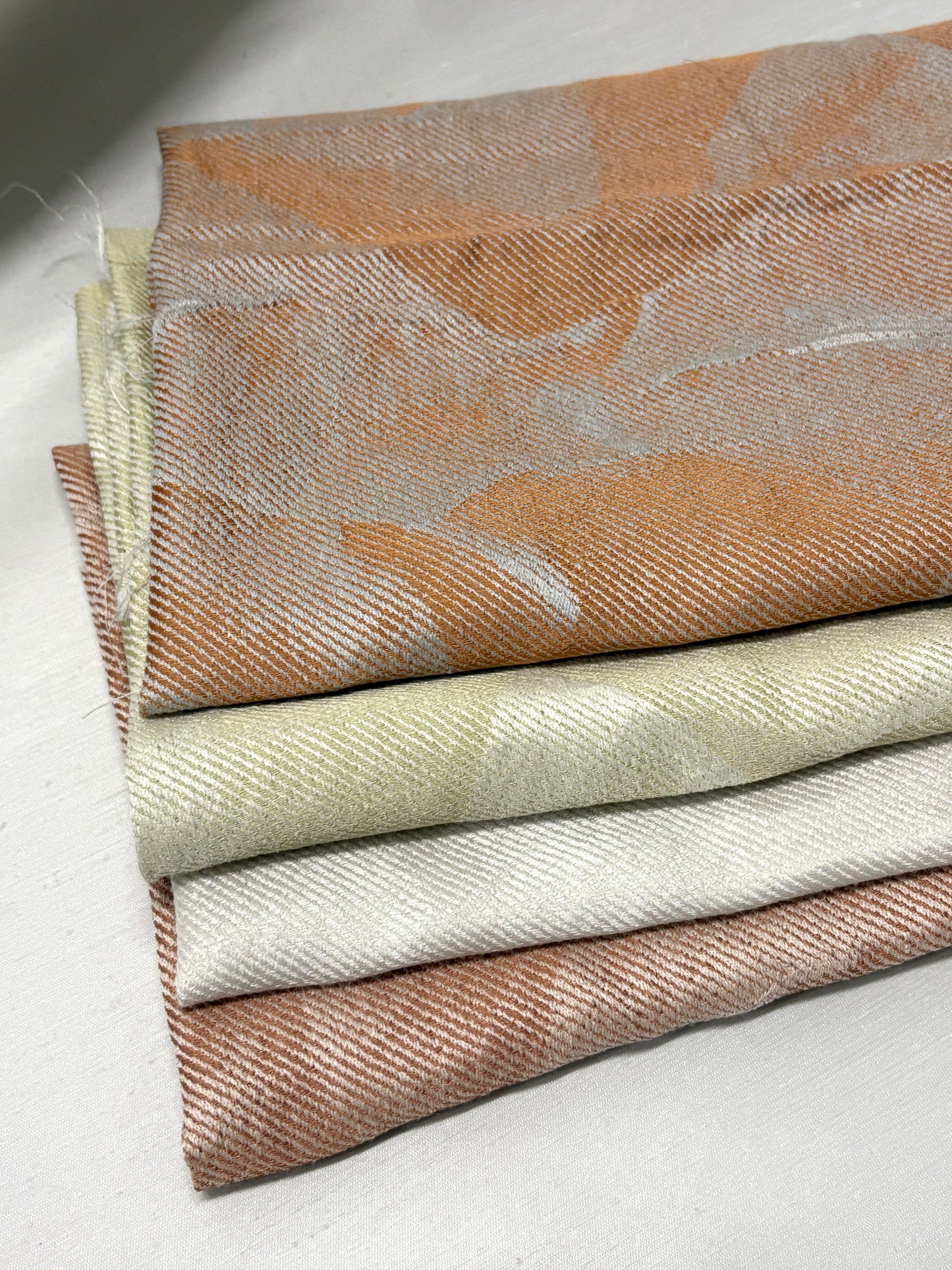 Hand holding folded fabric swatches in soft neutral tones.