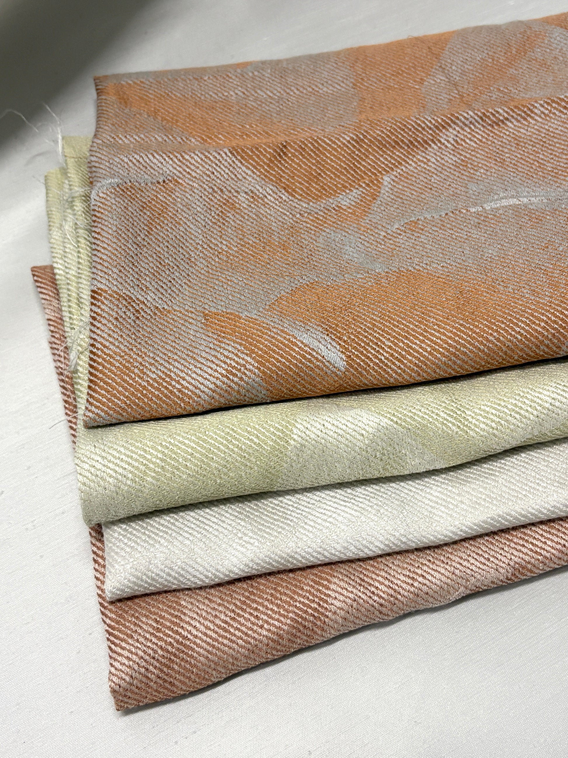 Hand holding folded fabric swatches in soft neutral tones.
