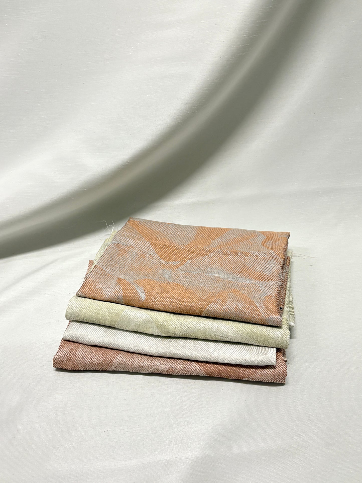Hand holding a stack of neutral fabric swatches on a light background.