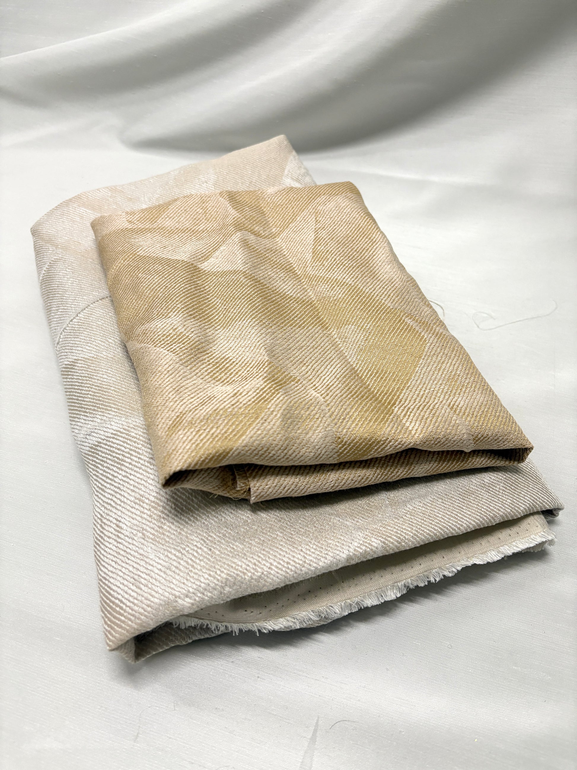 Folded neutral fabric pieces layered to show soft texture and subtle pattern.