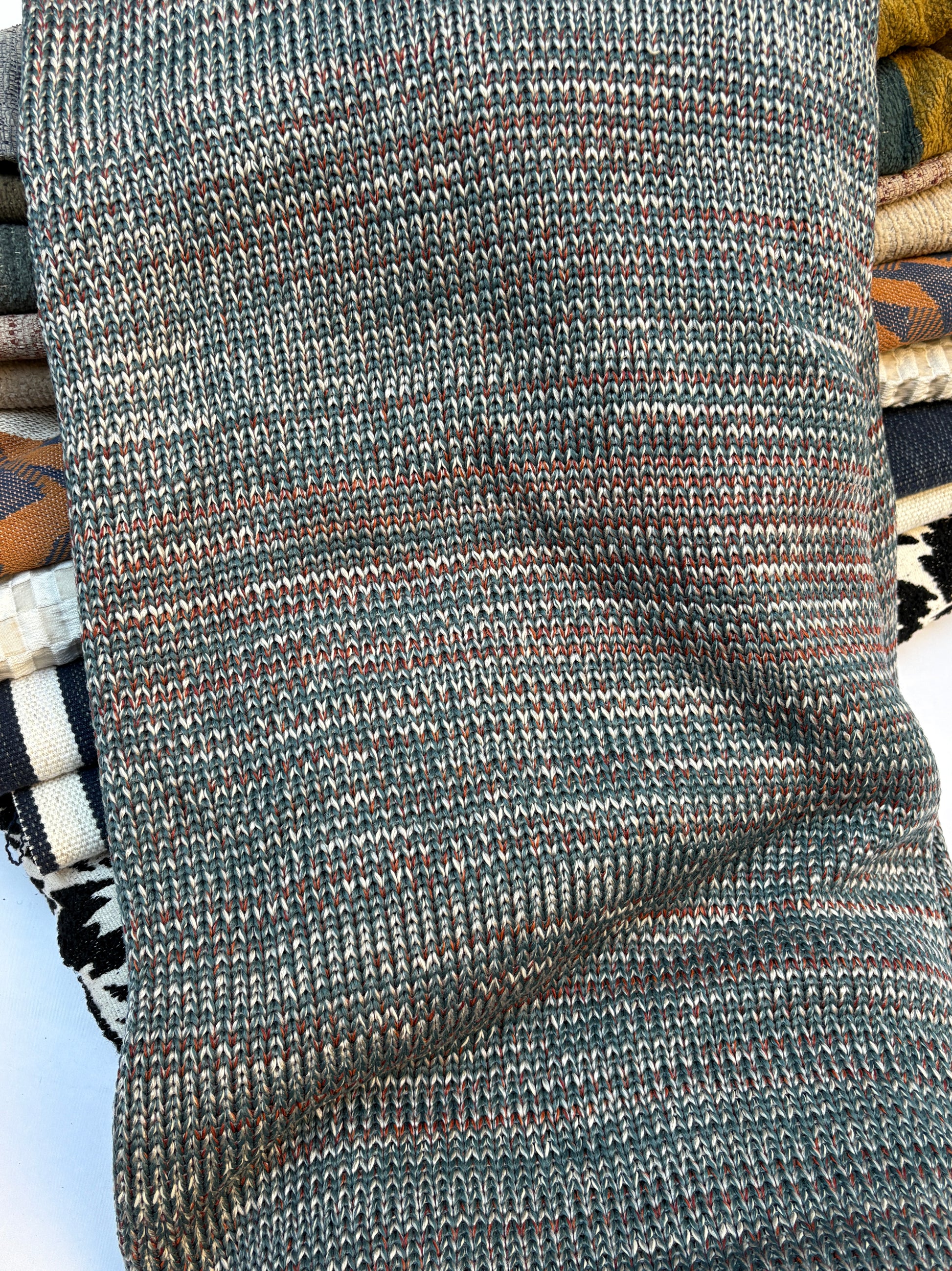 Close-up of a textured fabric with horizontal stripes in dark green, orange, brown, and white.