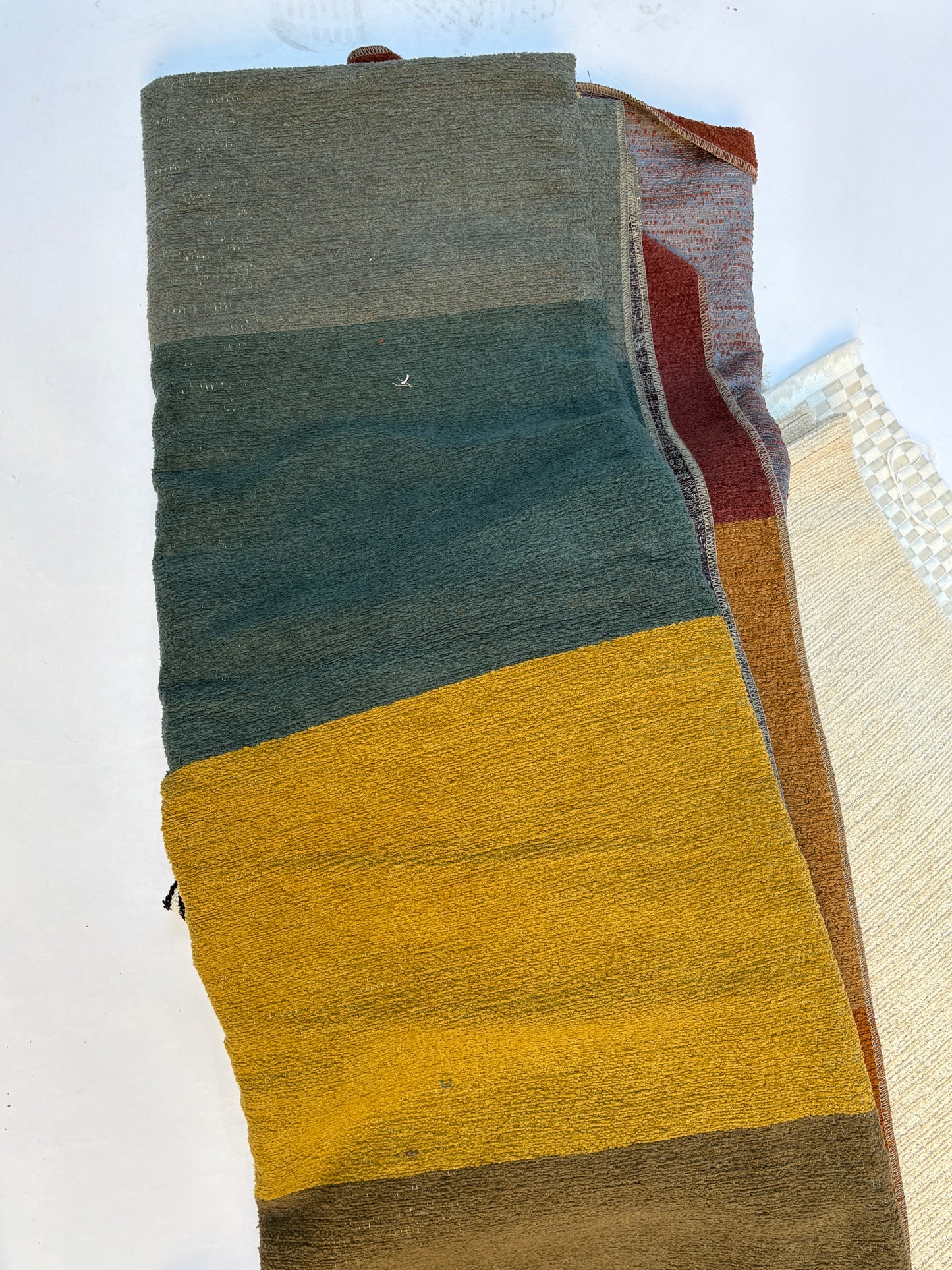 Folded, textured fabric with bold stripes in light grey, green, yellow, and brown 