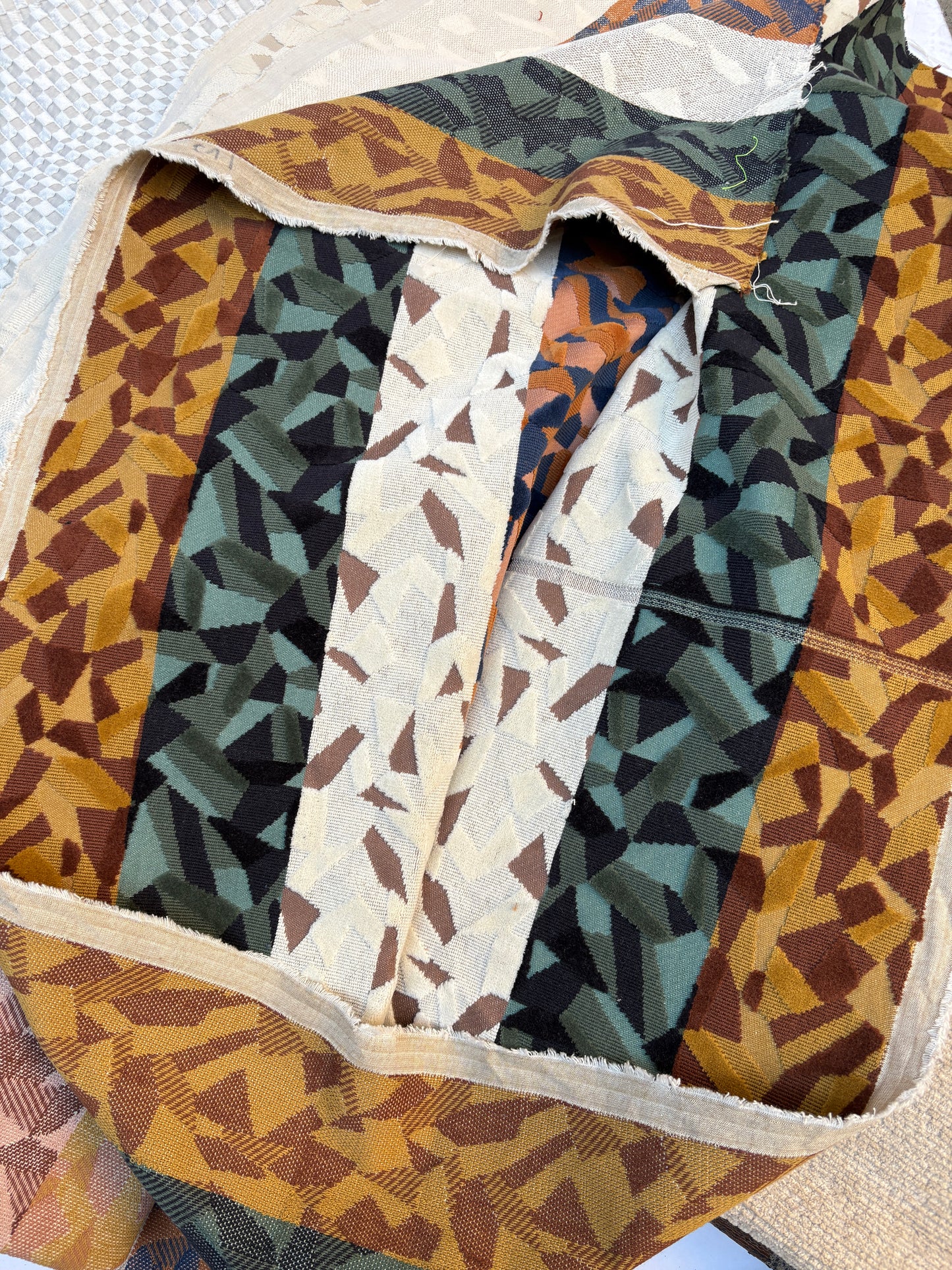 Textured fabric with three thick stripes in orange, green, and white. Each stripe features a geometric pattern.