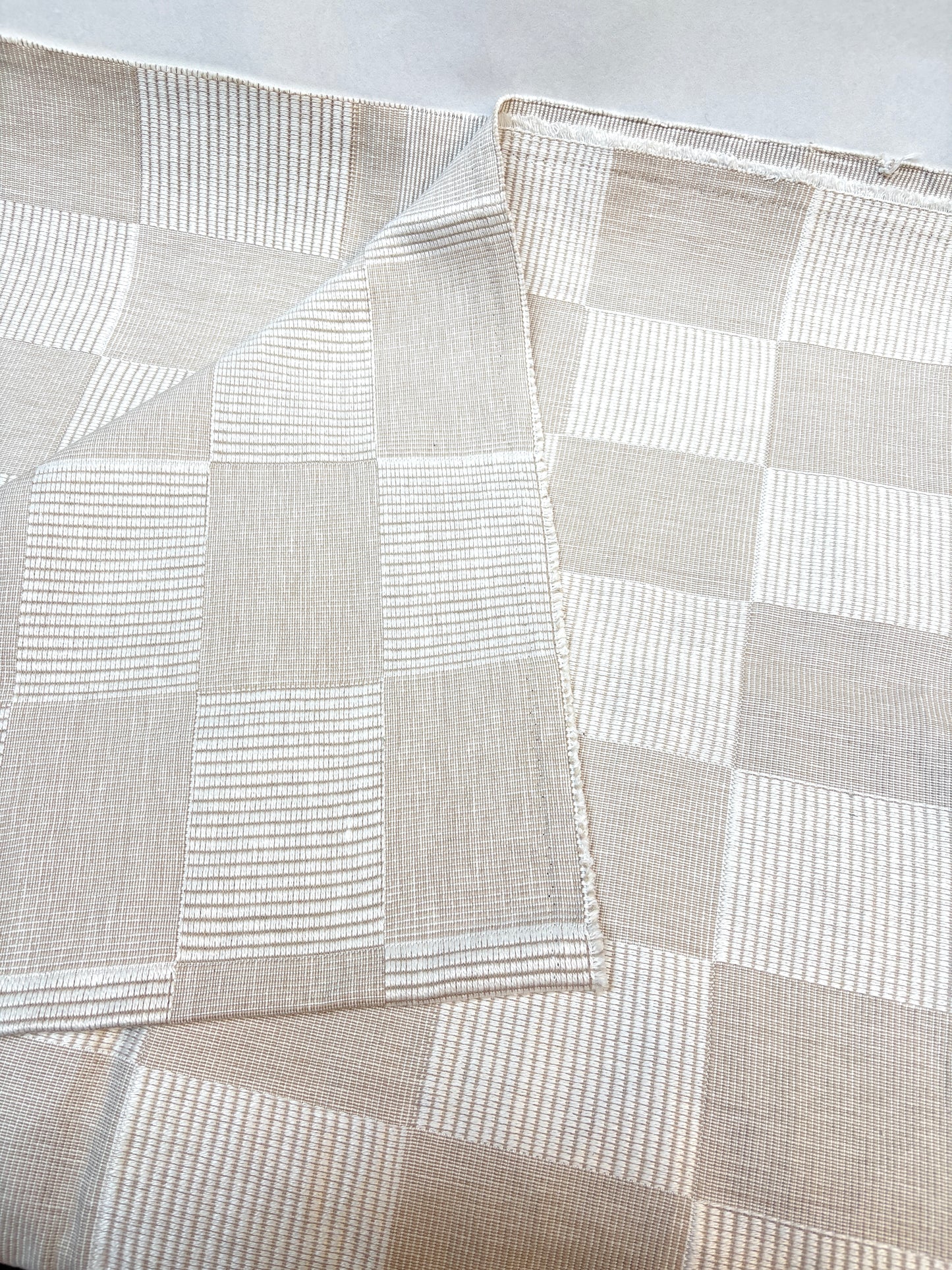 Close-up of layered cream checkered fabric pieces on a white background.
