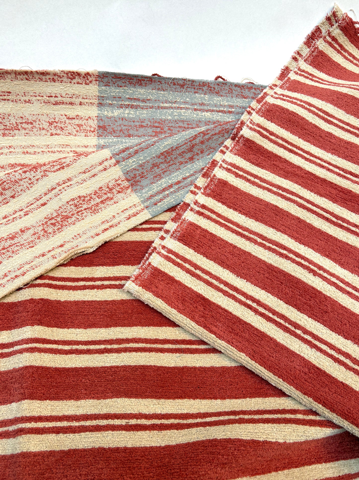 Layered striped fabric pieces in red, cream and muted blue tones.