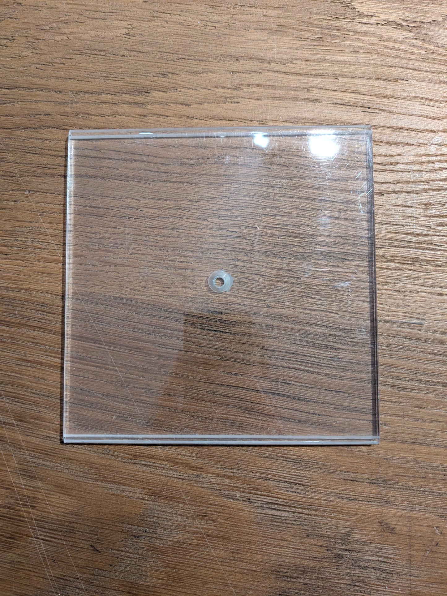 Clear square plastic sheet with a small hole in the middle on a wooden surface. 