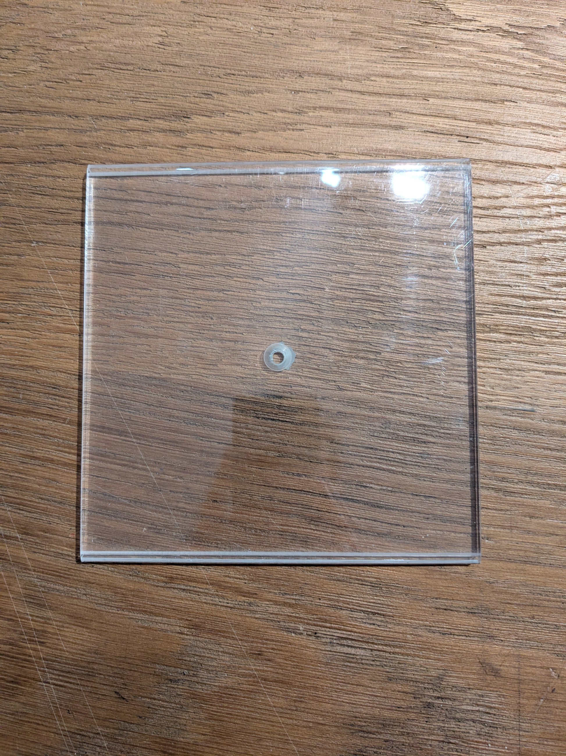 Clear square plastic sheet with a small hole in the middle on a wooden surface. 